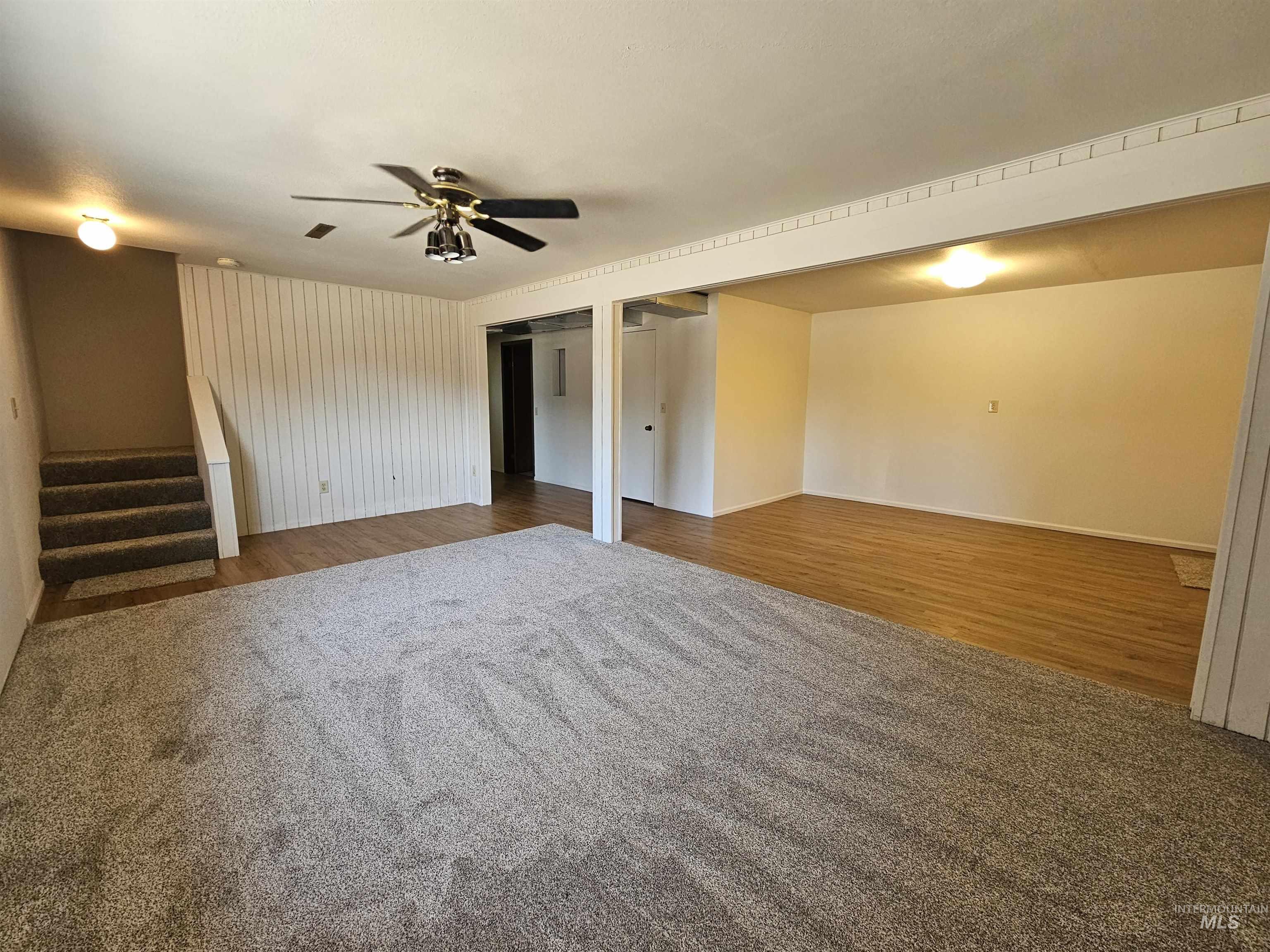 Unfurnished living room with stairs, wood finished floors, ceiling fan, and carpet