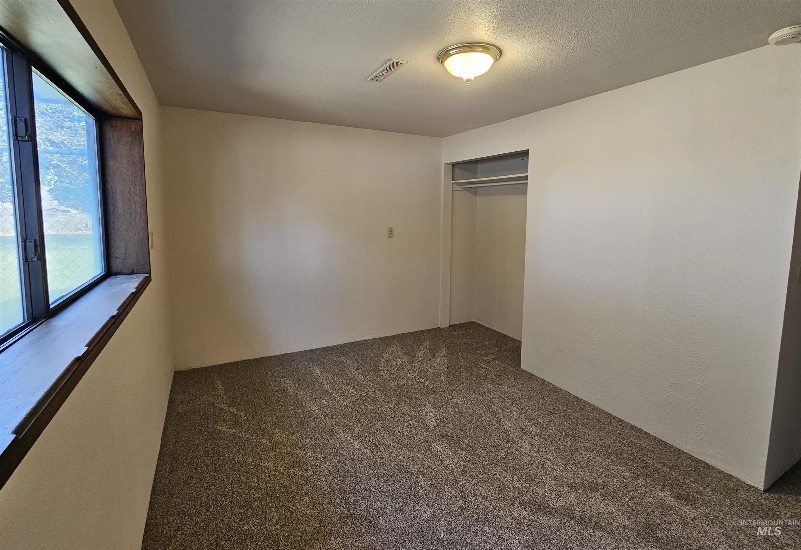 Unfurnished bedroom featuring dark carpet, a closet, and a textured ceiling