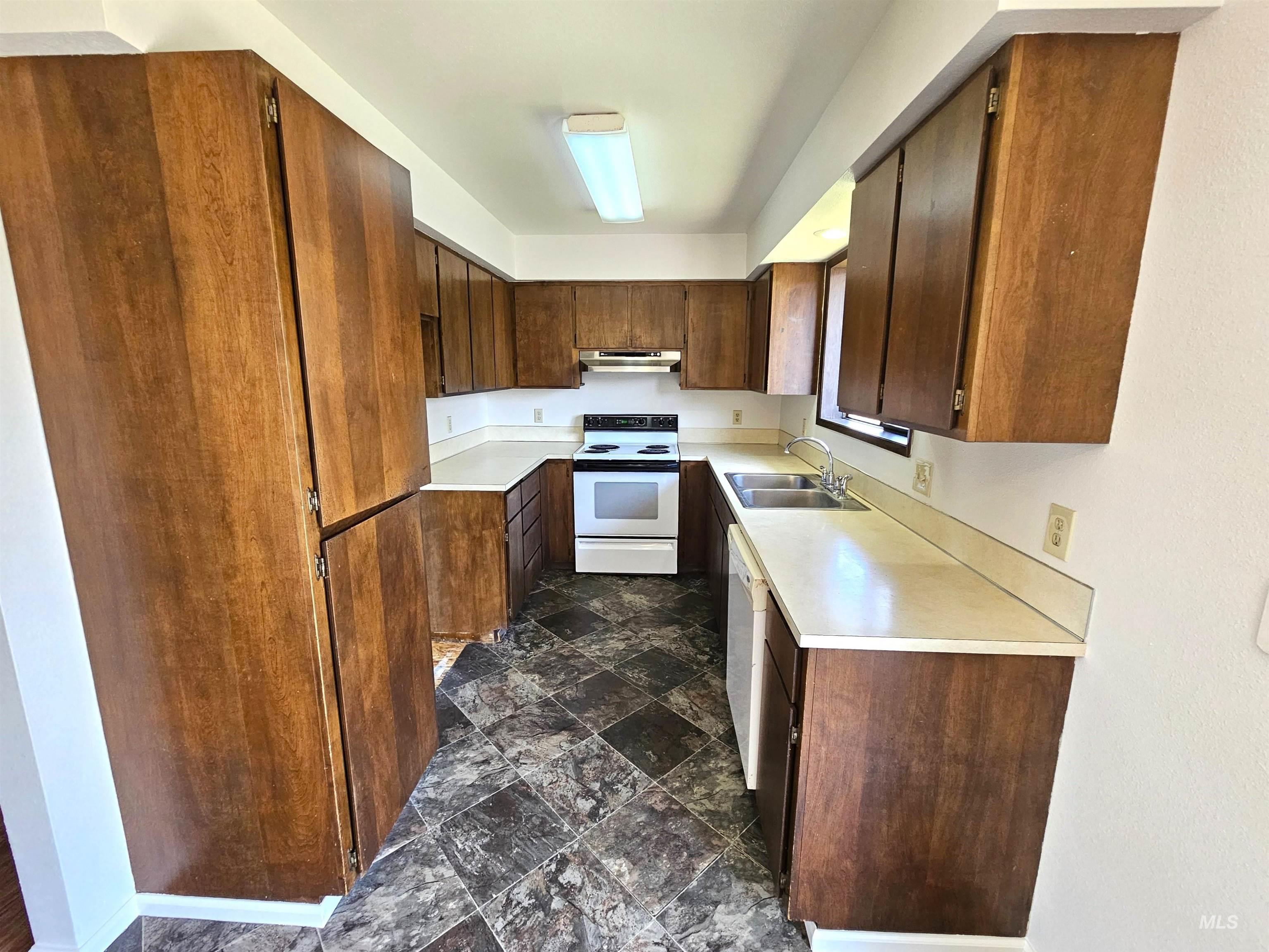 Kitchen featuring light countertops, stone finish flooring, white appliances, and under cabinet range hood