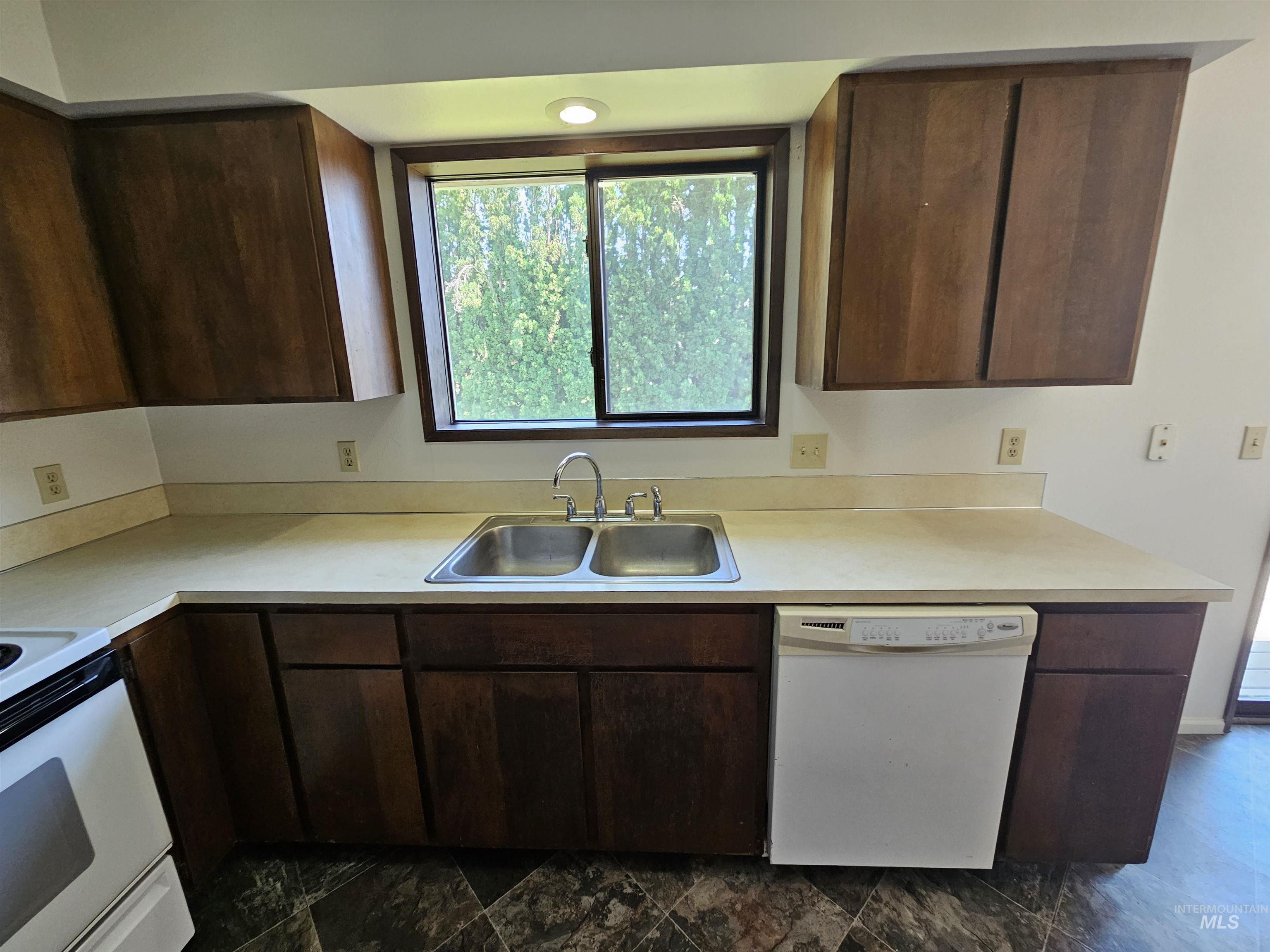 Kitchen featuring dark brown cabinetry, white appliances, and light countertops