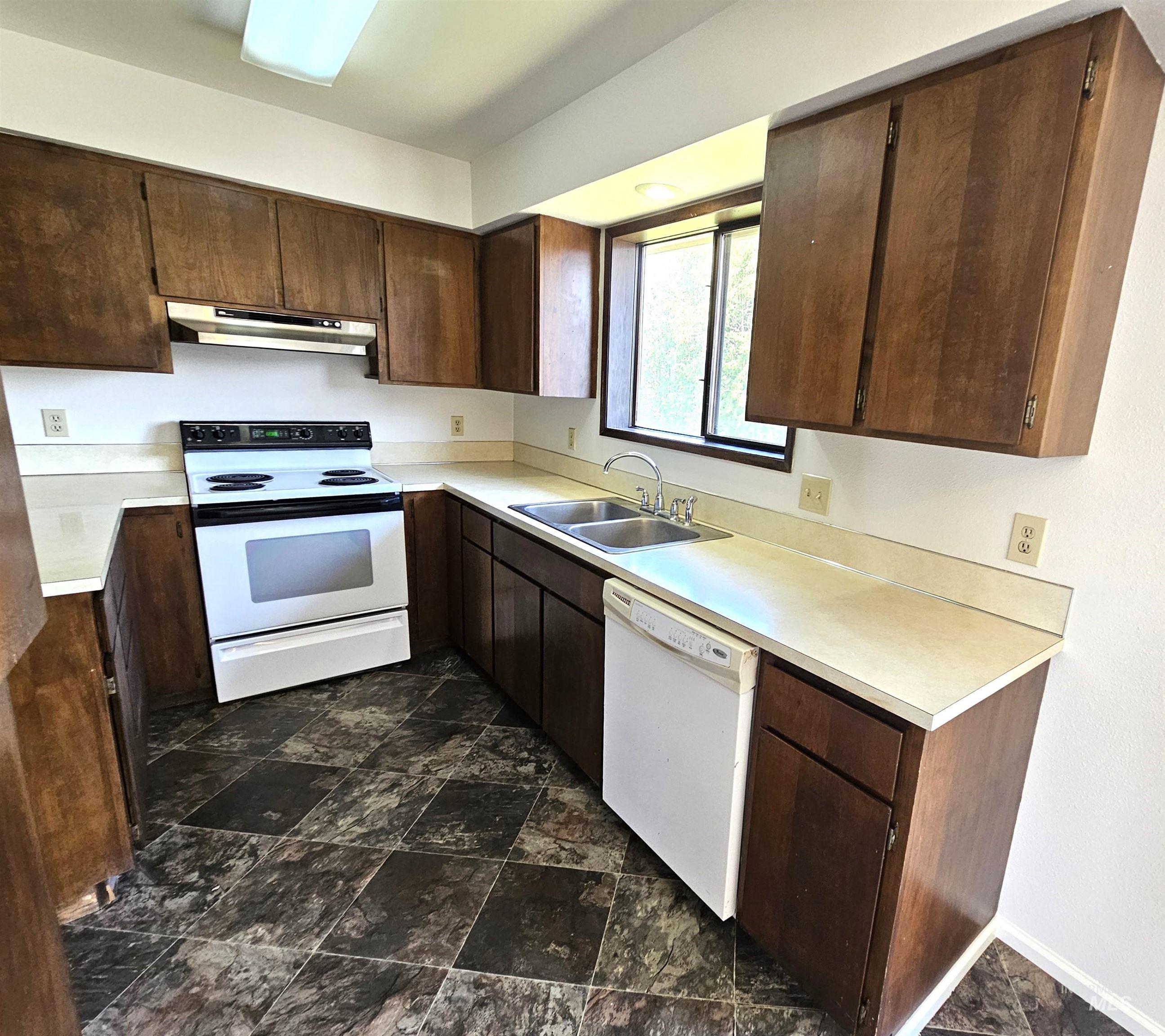 Kitchen featuring white appliances, dark brown cabinets, stone finish flooring, and light countertops