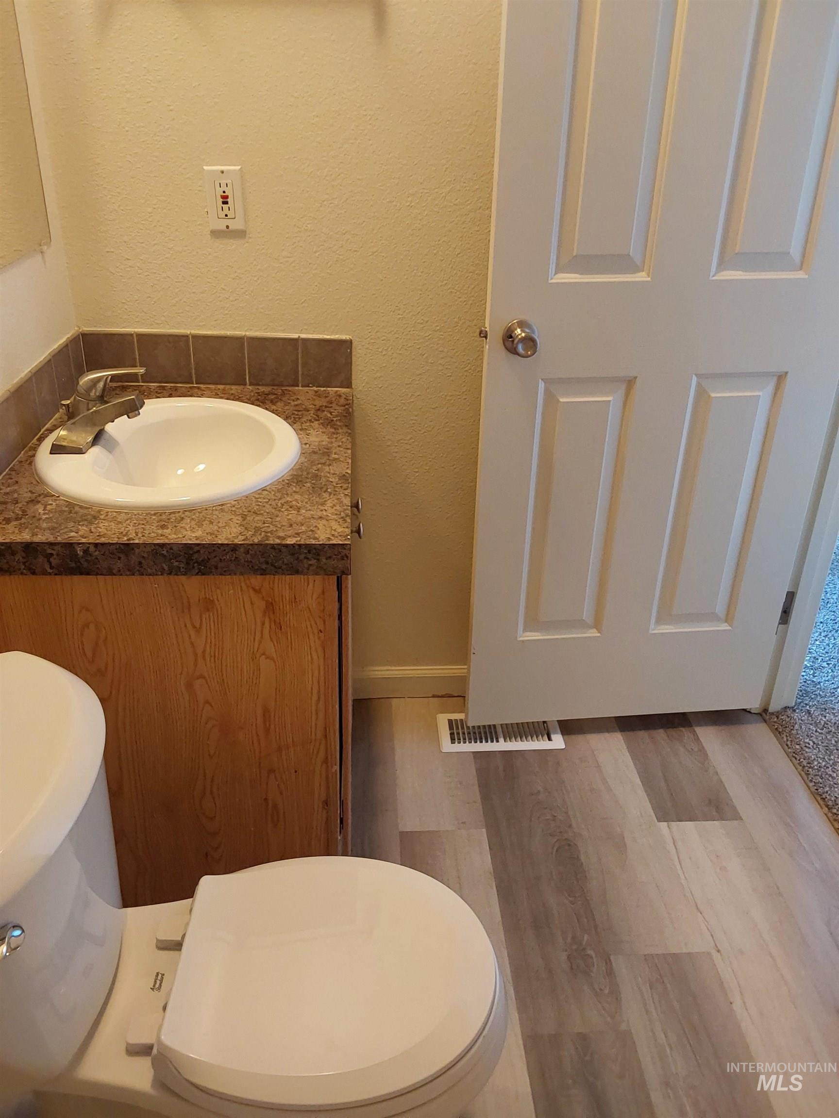 Half bathroom with a textured wall, vanity, and wood finished floors