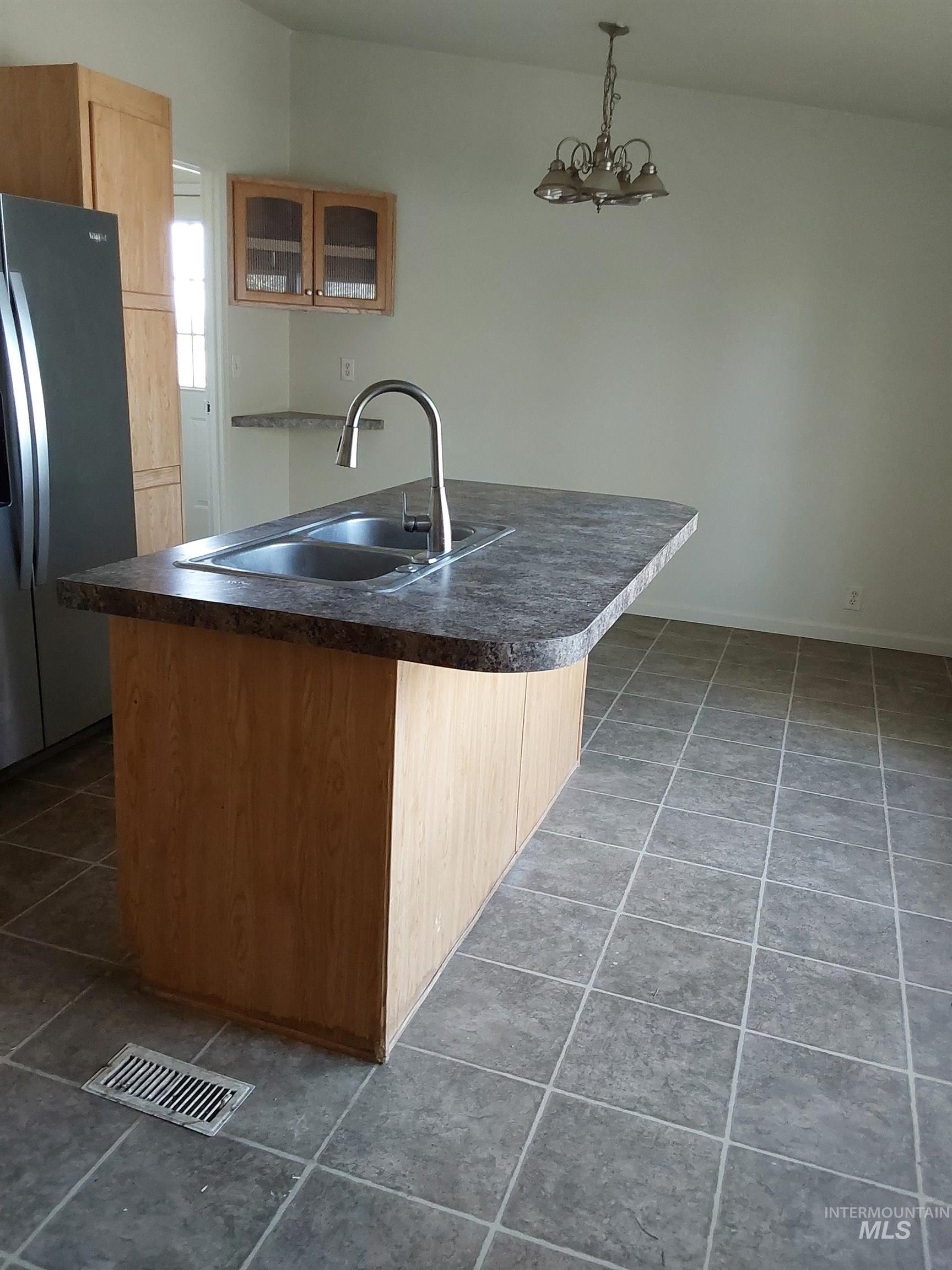 Kitchen featuring glass insert cabinets, freestanding refrigerator, dark countertops, decorative light fixtures, and dark tile patterned flooring