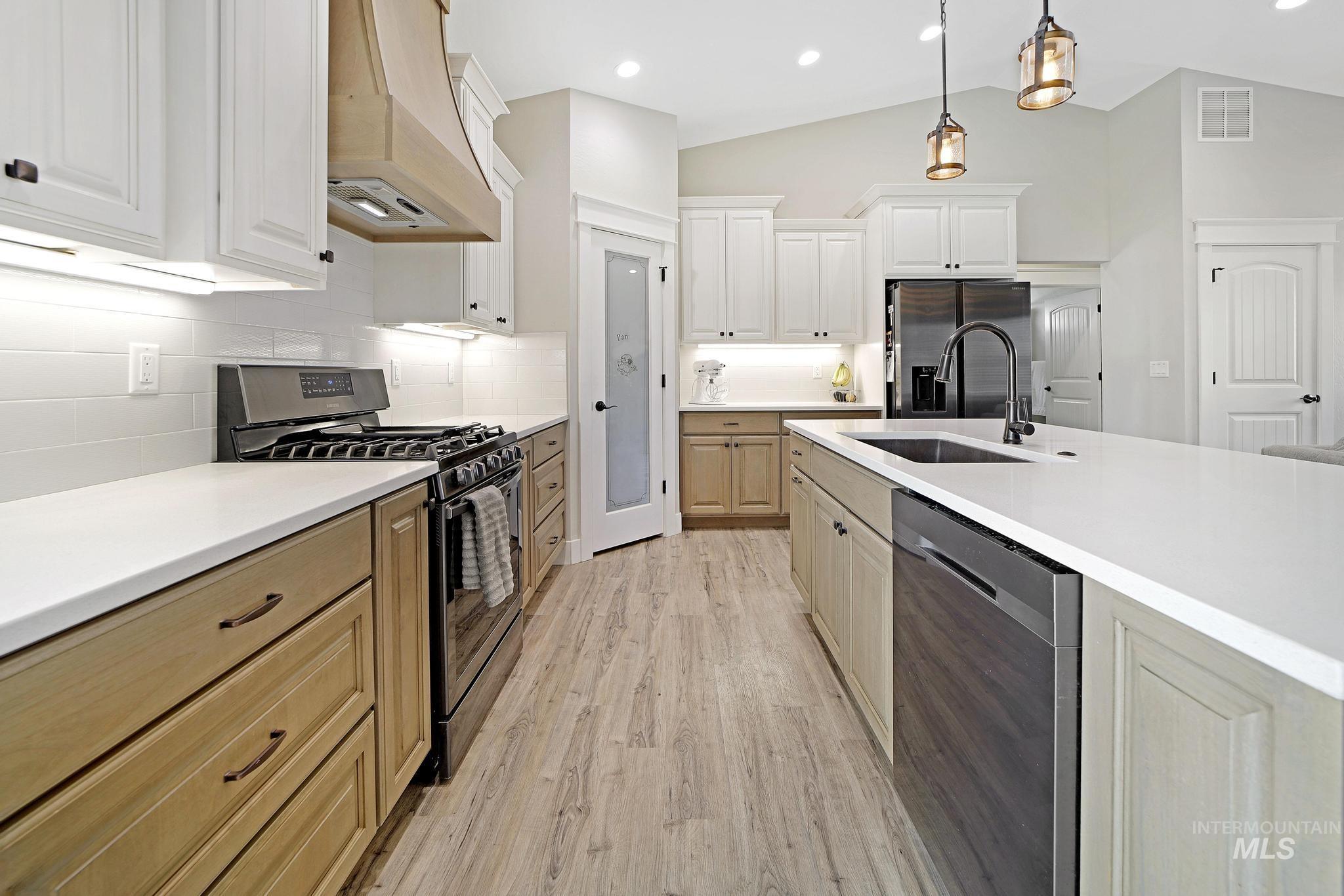 Kitchen with appliances with stainless steel finishes, premium range hood, decorative backsplash, light wood-type flooring, and hanging light fixtures