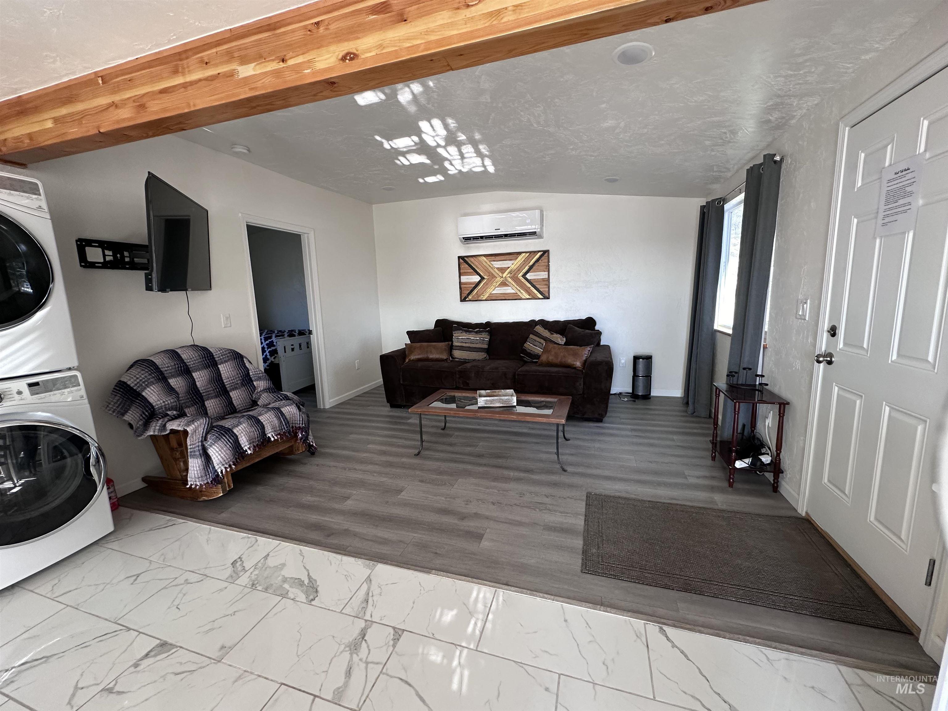 Living room featuring light marble finish flooring, stacked washer / drying machine, and beamed ceiling