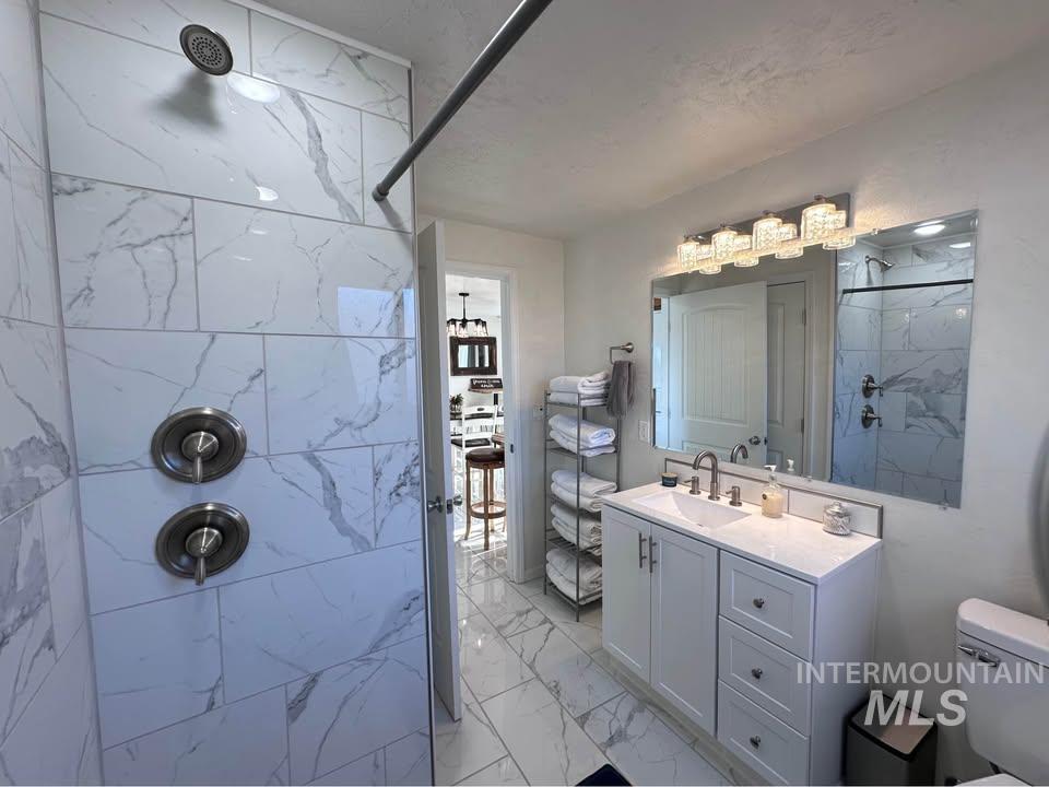 Bathroom featuring light marble finish flooring, a marble finish shower, and vanity