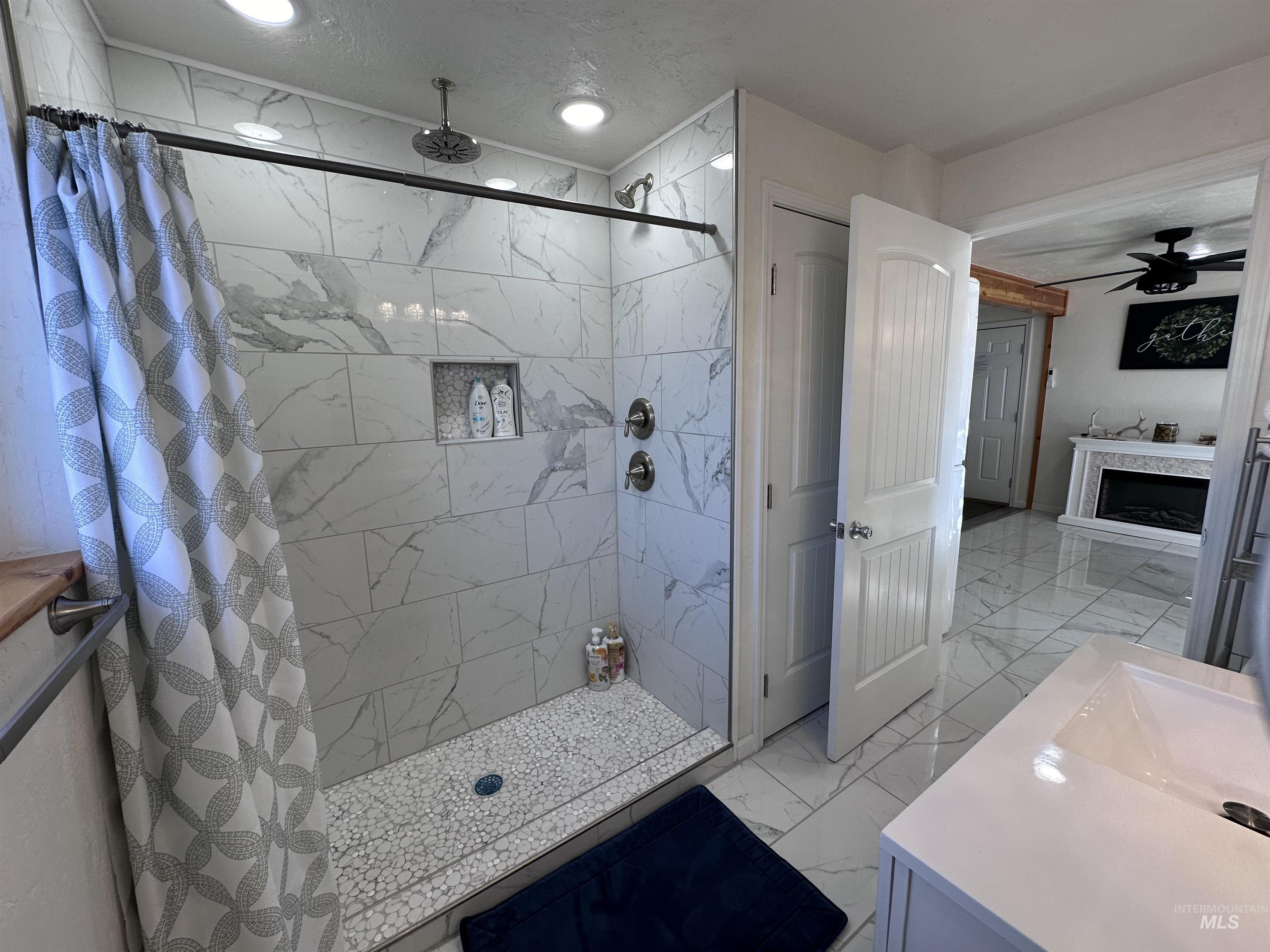 Full bath with ceiling fan, light marble finish flooring, a shower stall, vanity, and a textured ceiling