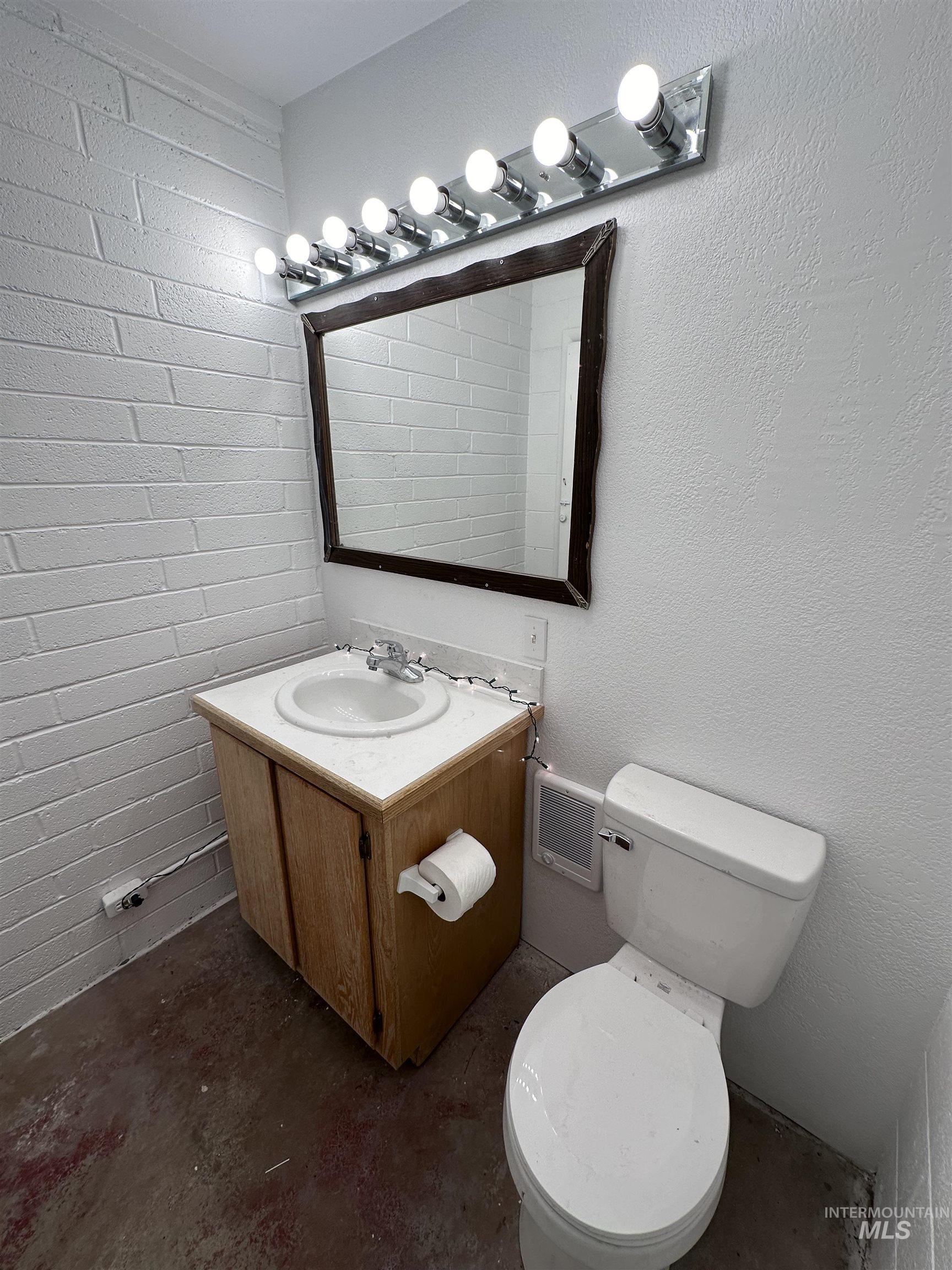 Bathroom with concrete floors, vanity, and a textured wall