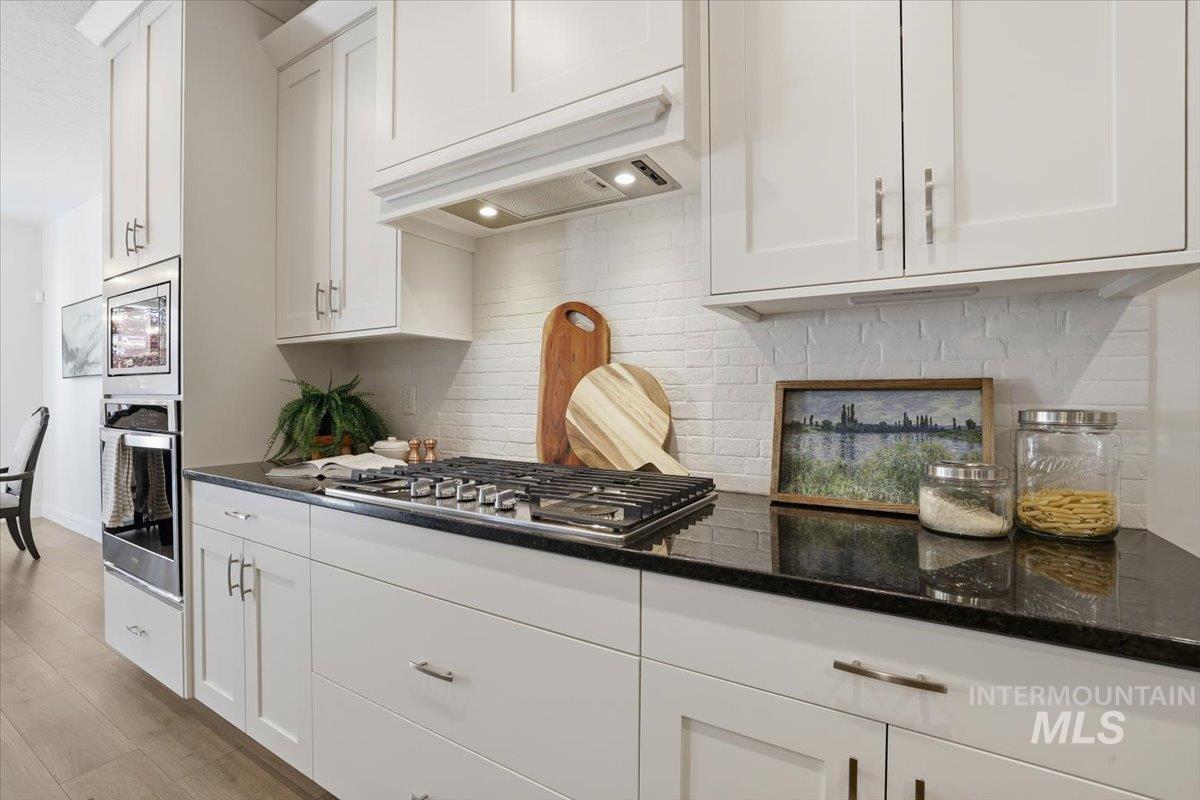 Kitchen featuring tasteful backsplash, white cabinetry, appliances with stainless steel finishes, and custom exhaust hood