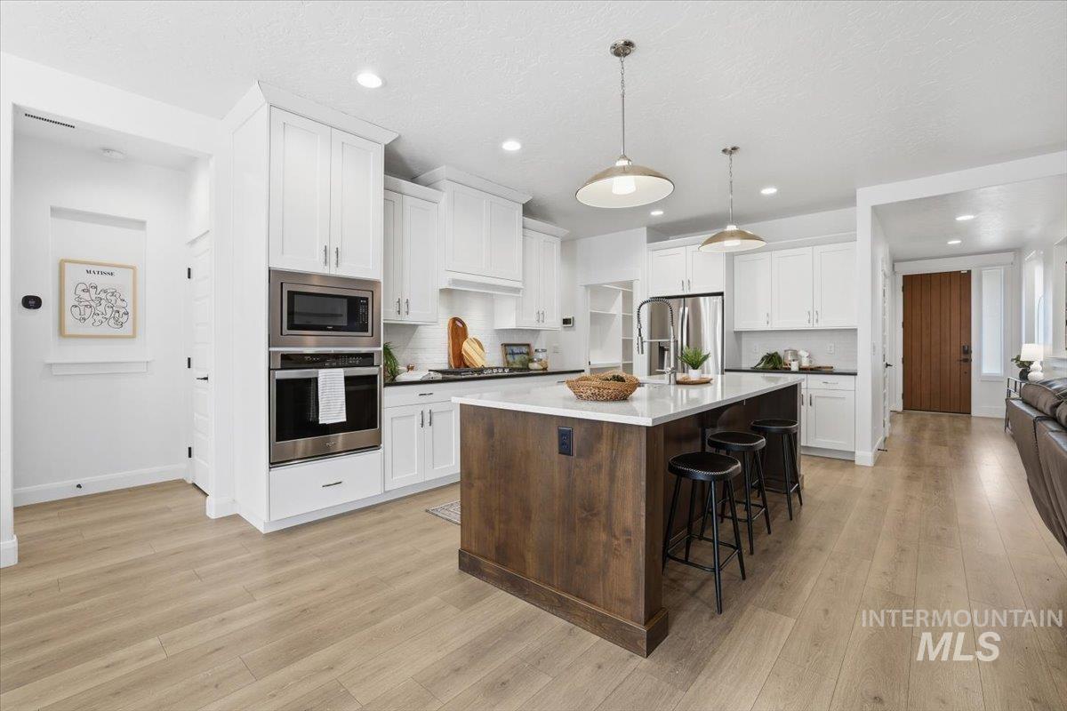 Kitchen with white cabinetry, appliances with stainless steel finishes, a kitchen bar, tasteful backsplash, and a kitchen island with sink