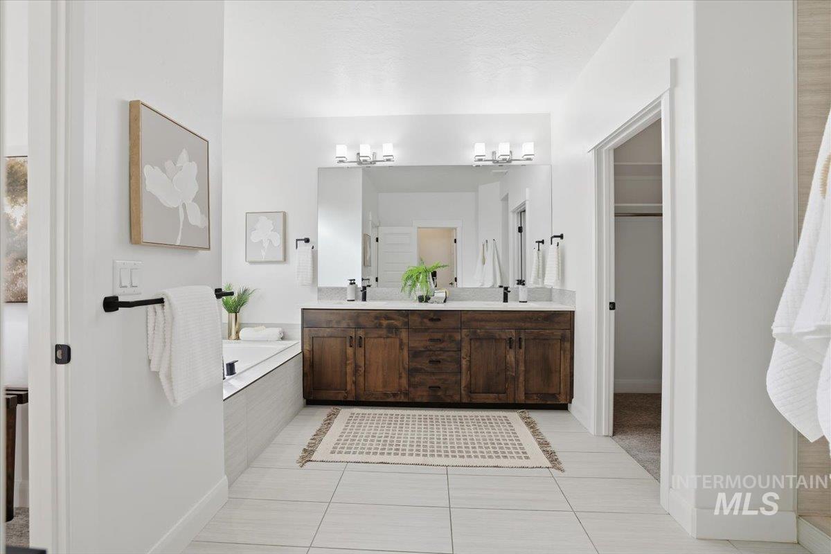 Bathroom with light tile patterned floors, a walk in closet, double vanity, and a garden tub