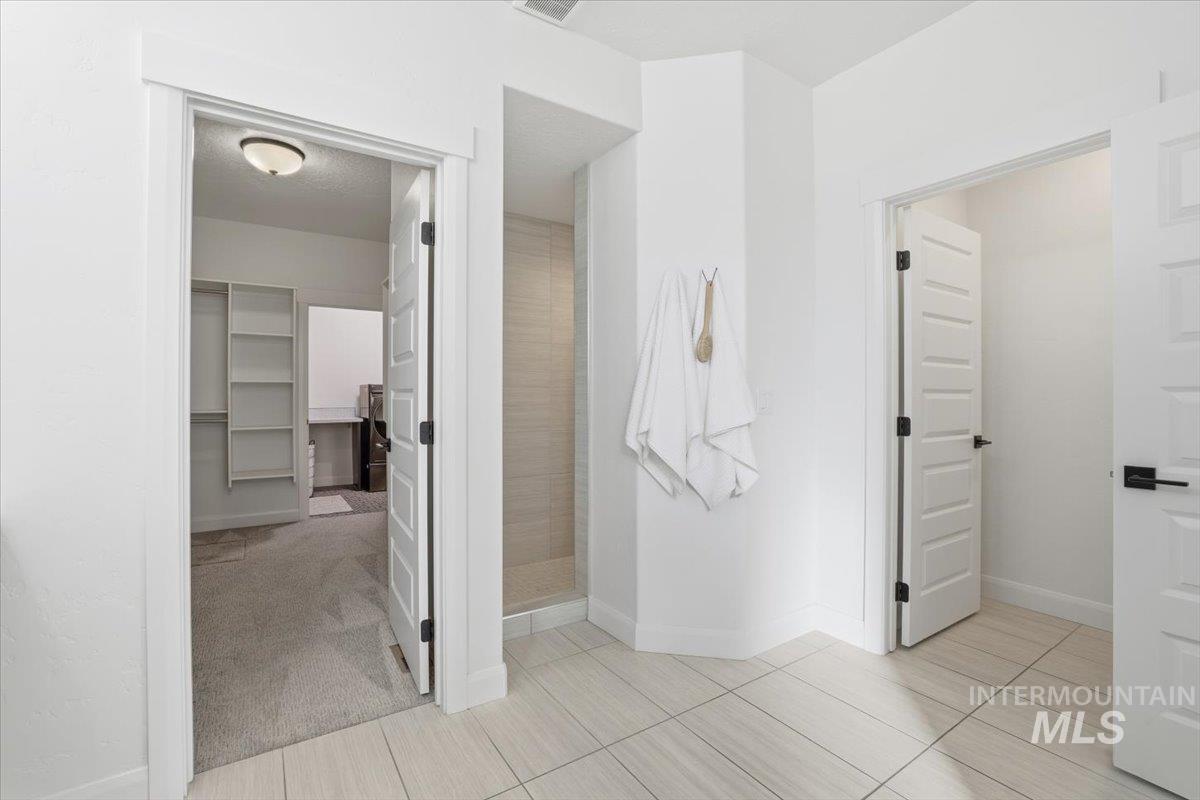 Bathroom with a spacious closet, light tile patterned floors, light colored carpet, and tiled shower