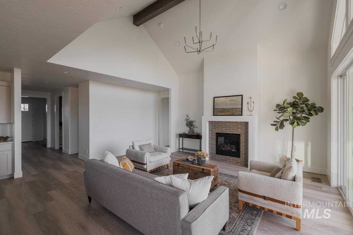 Living room featuring high vaulted ceiling, beam ceiling, wood finished floors, and a fireplace