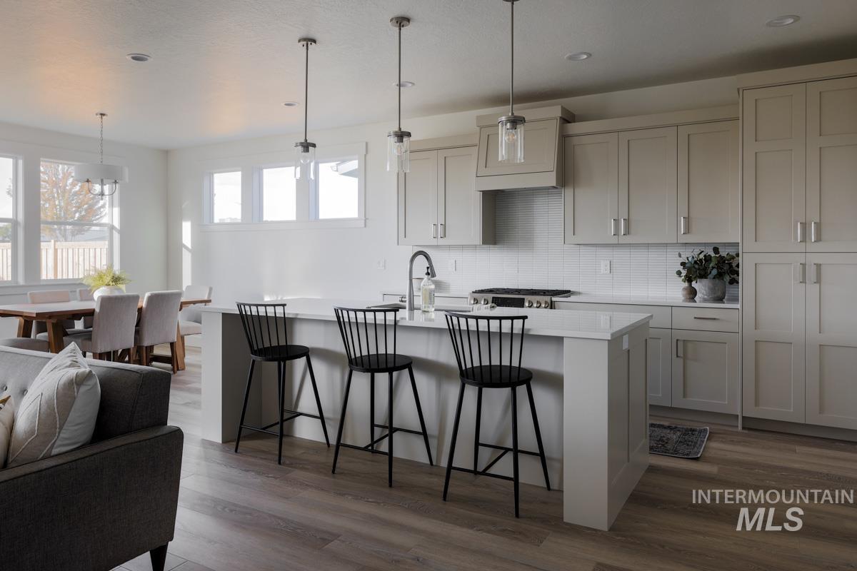 Kitchen featuring decorative backsplash, pendant lighting, a kitchen breakfast bar, a center island with sink, and dark wood-type flooring