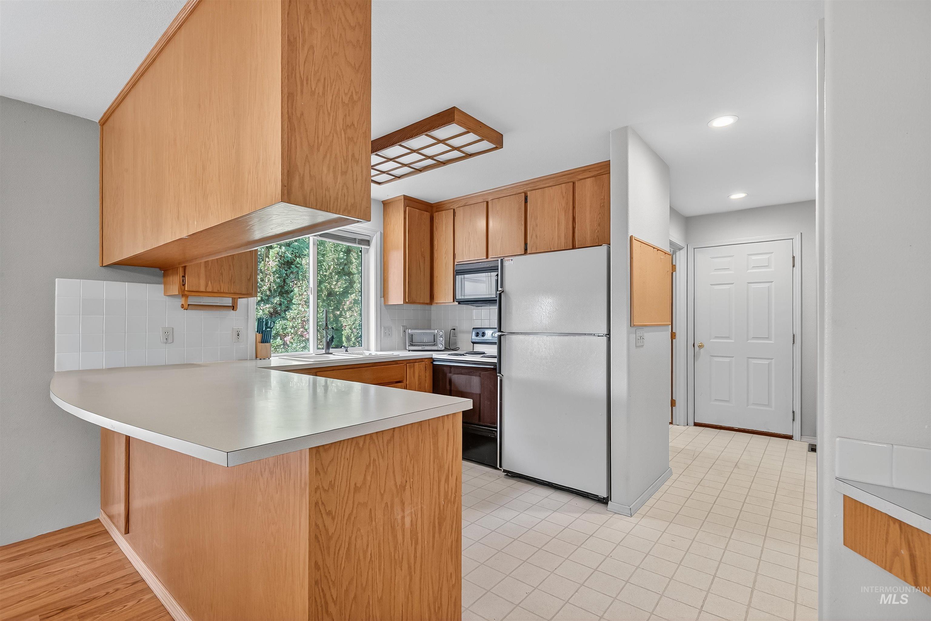 Kitchen featuring a peninsula, light countertops, freestanding refrigerator, electric stove, and decorative backsplash