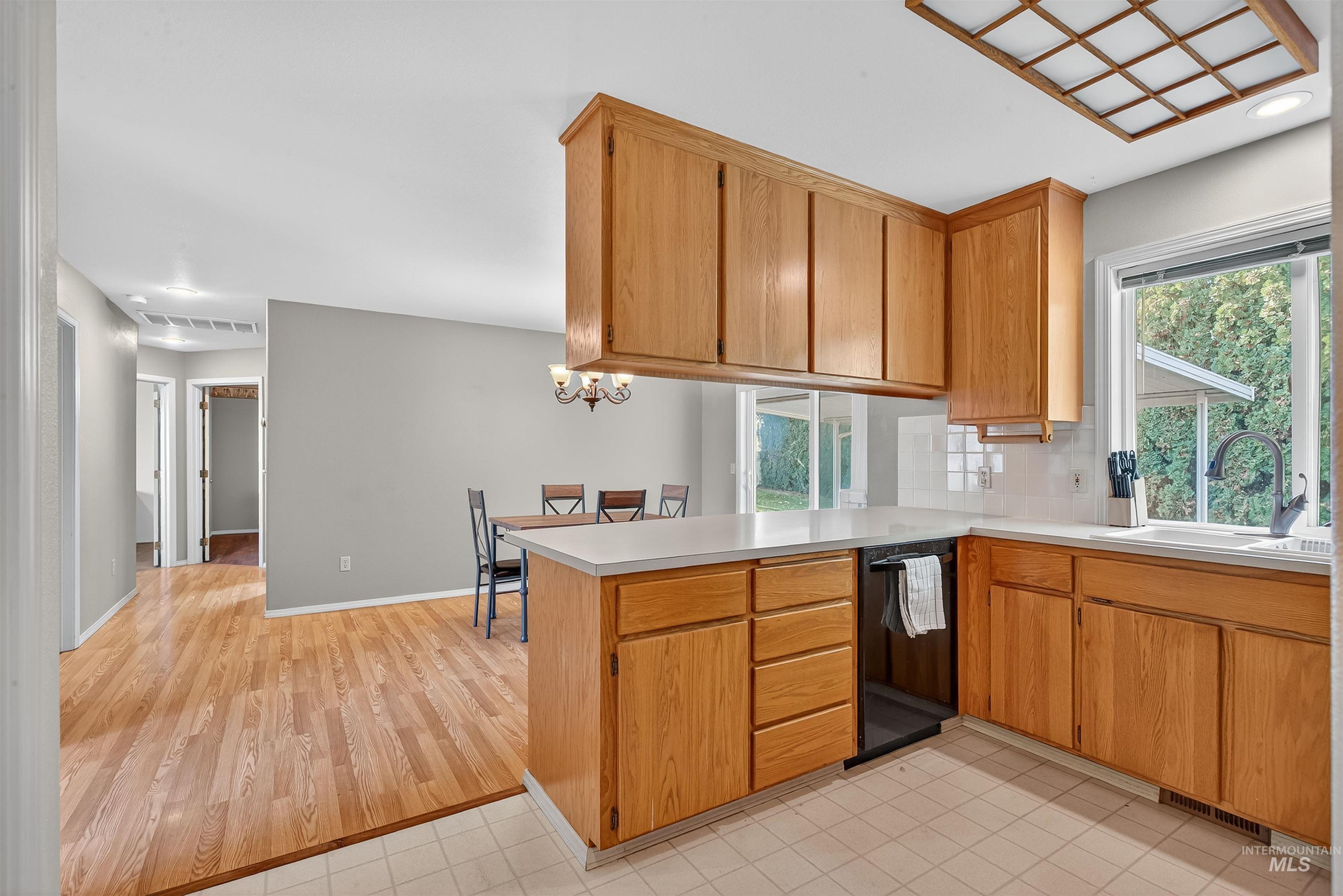 Kitchen with light countertops, a peninsula, brown cabinets, black dishwasher, and recessed lighting