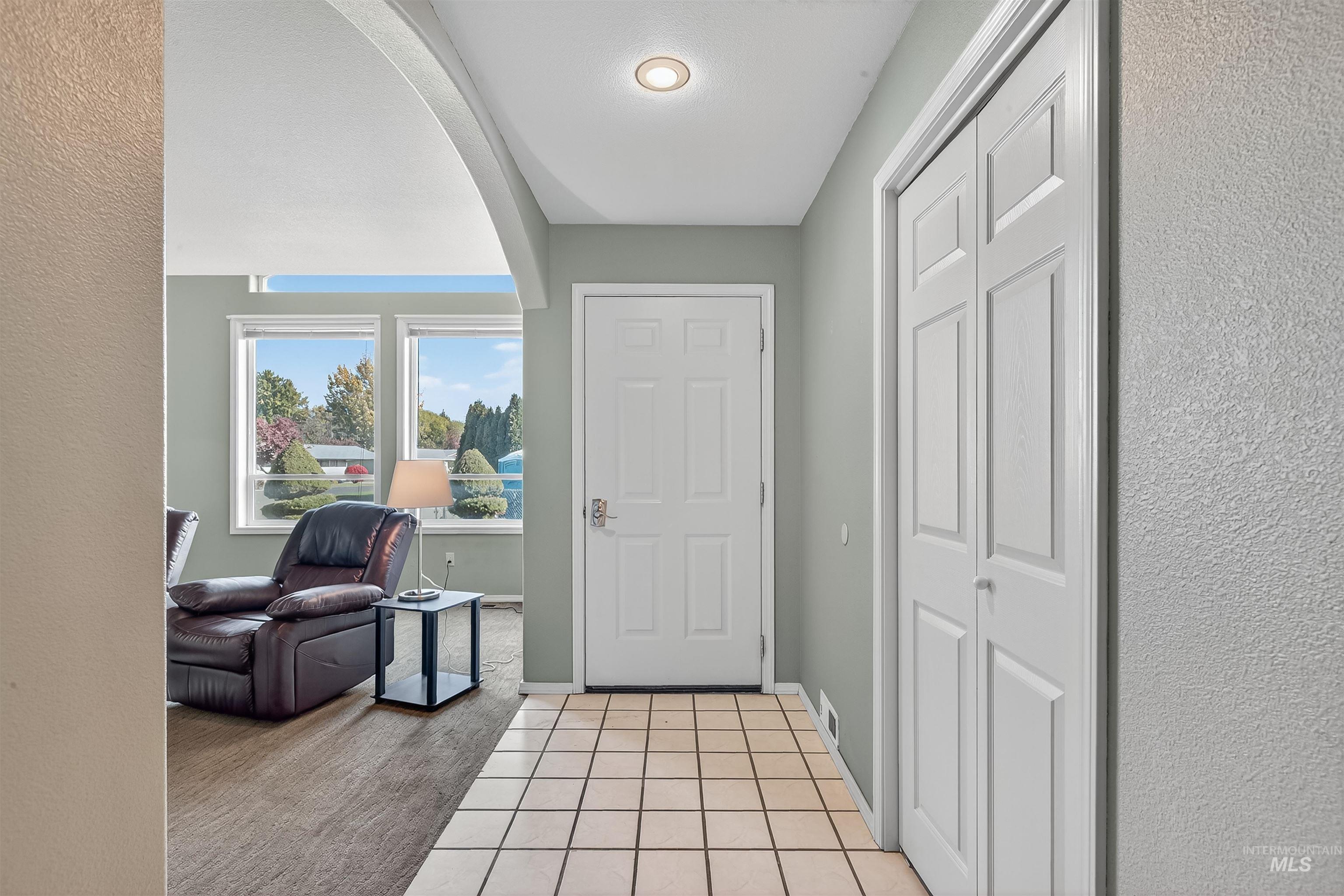Entryway with light tile patterned floors, arched walkways, light colored carpet, and a textured wall