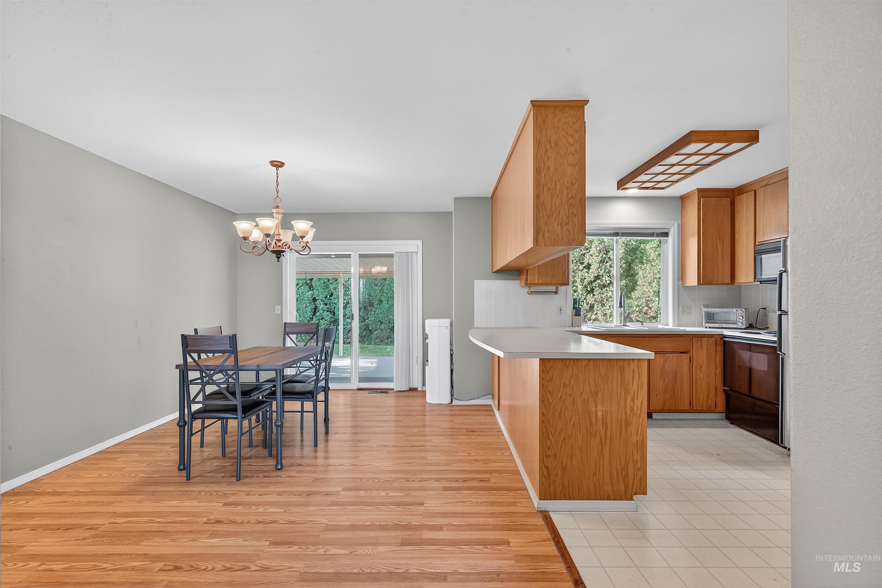 Kitchen with light countertops, a chandelier, tasteful backsplash, light wood-style flooring, and decorative light fixtures