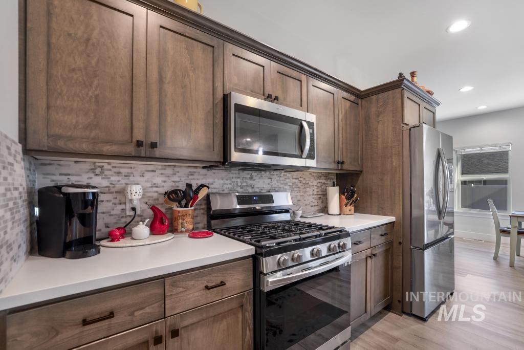 Kitchen with stainless steel appliances, decorative backsplash, light wood finished floors, recessed lighting, and dark brown cabinetry