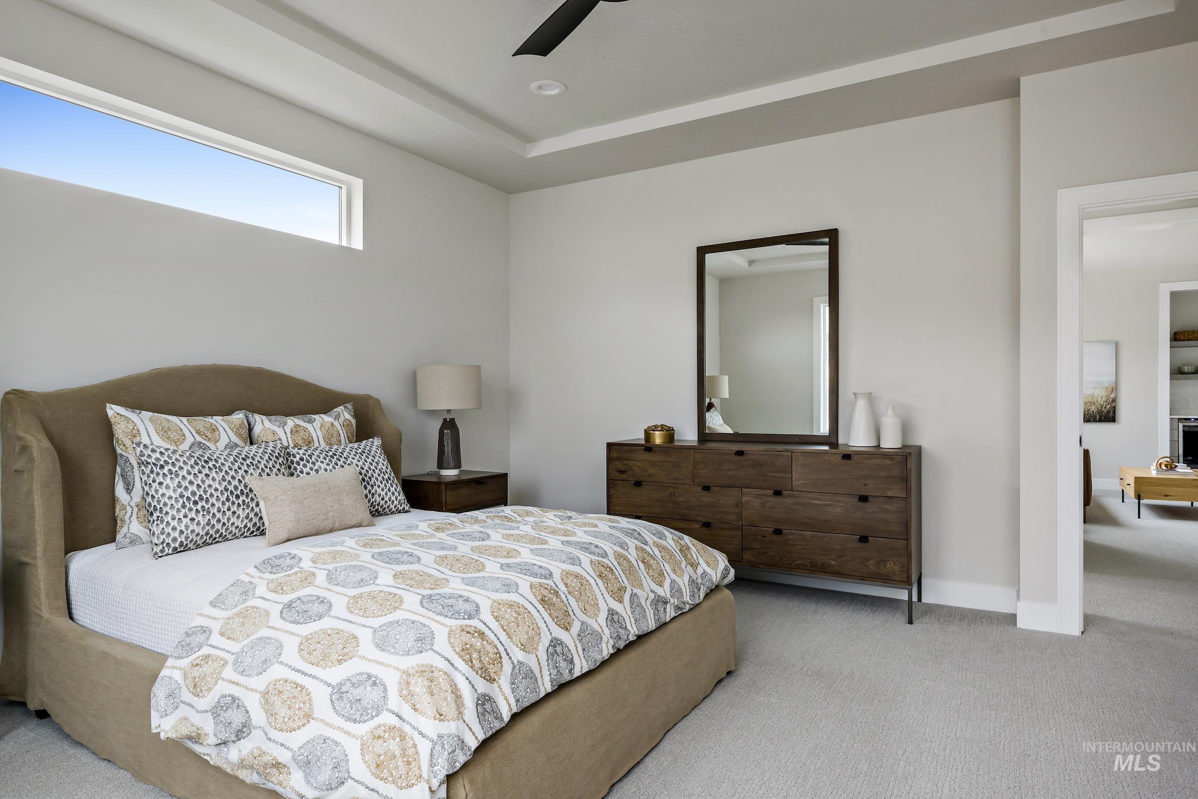 Carpeted bedroom featuring a ceiling fan and a raised ceiling