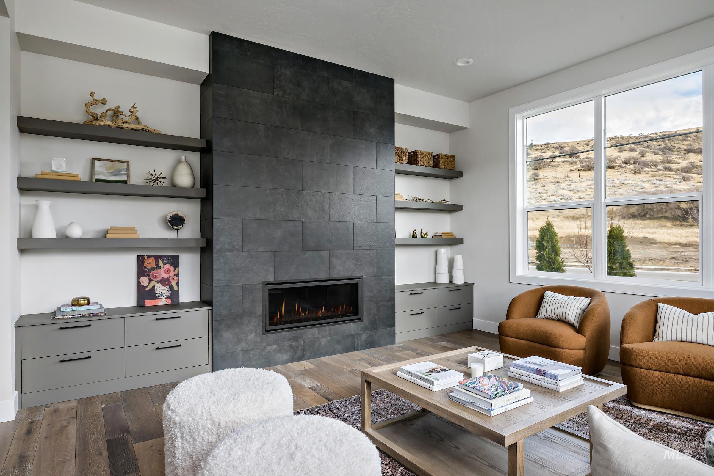Living room with dark wood-style flooring, a tiled fireplace, and built in shelves