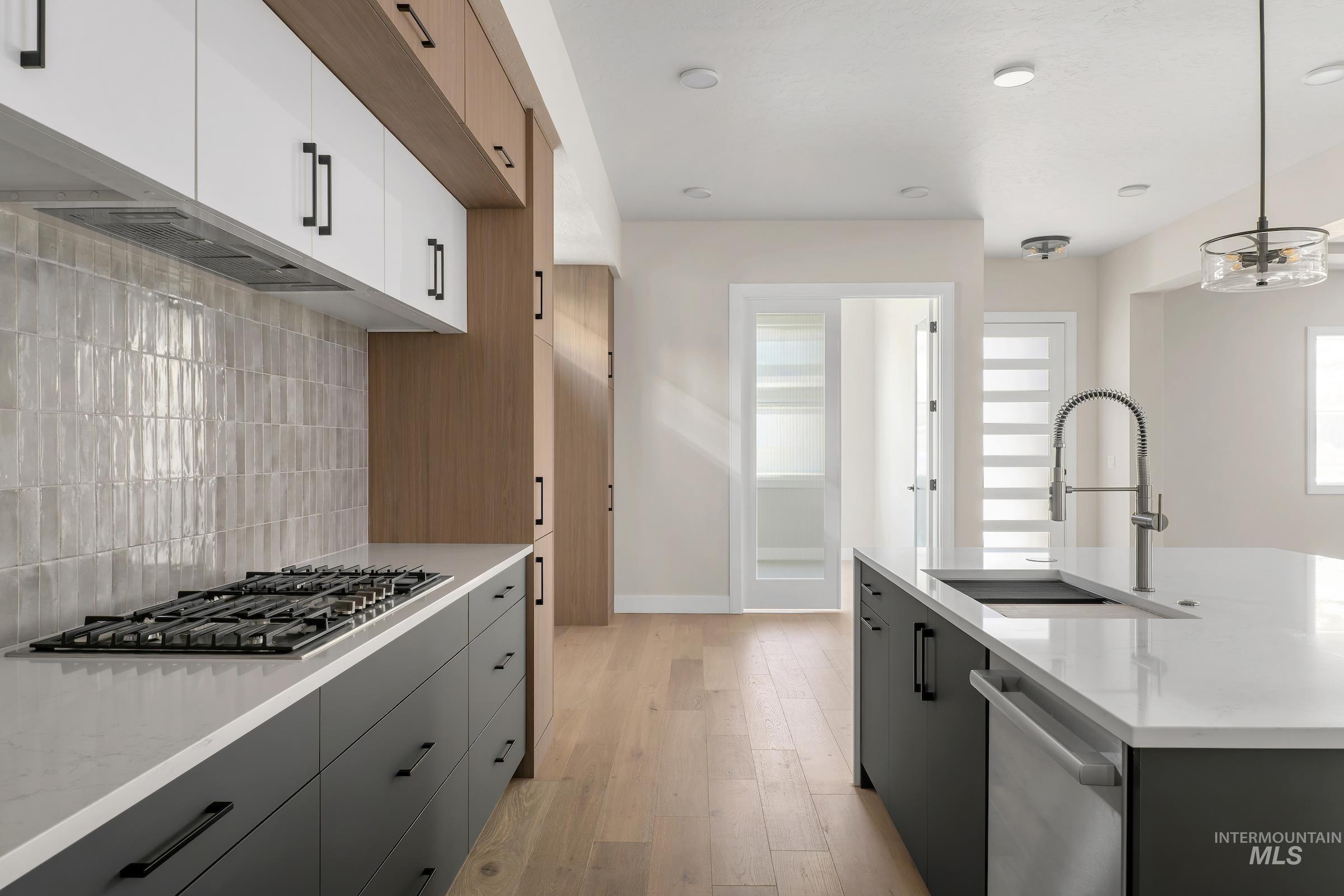 Kitchen featuring light wood finished floors, light stone counters, appliances with stainless steel finishes, tasteful backsplash, and decorative light fixtures