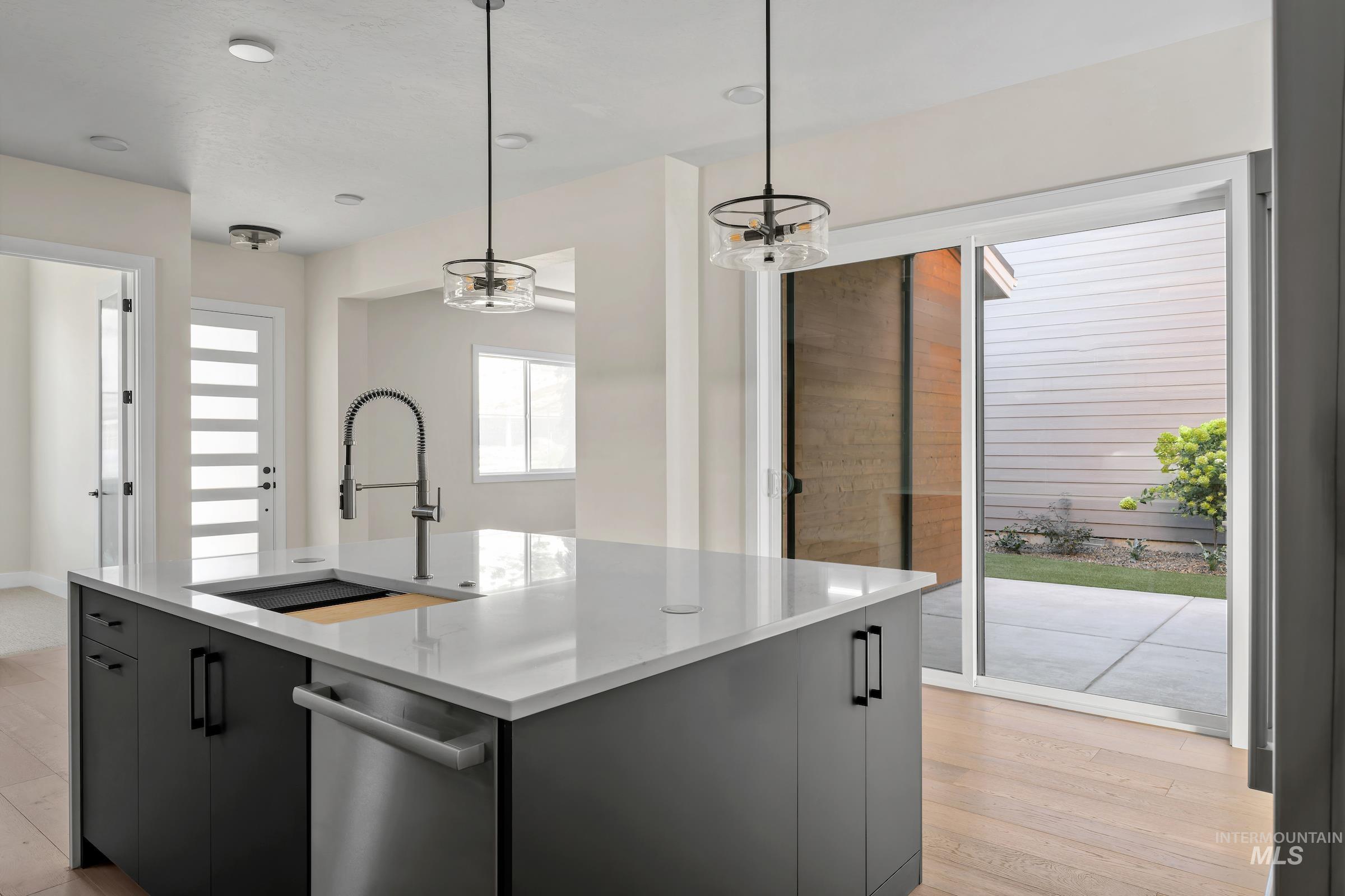 Kitchen featuring pendant lighting, a kitchen island with sink, modern cabinets, stainless steel dishwasher, and light wood-style flooring