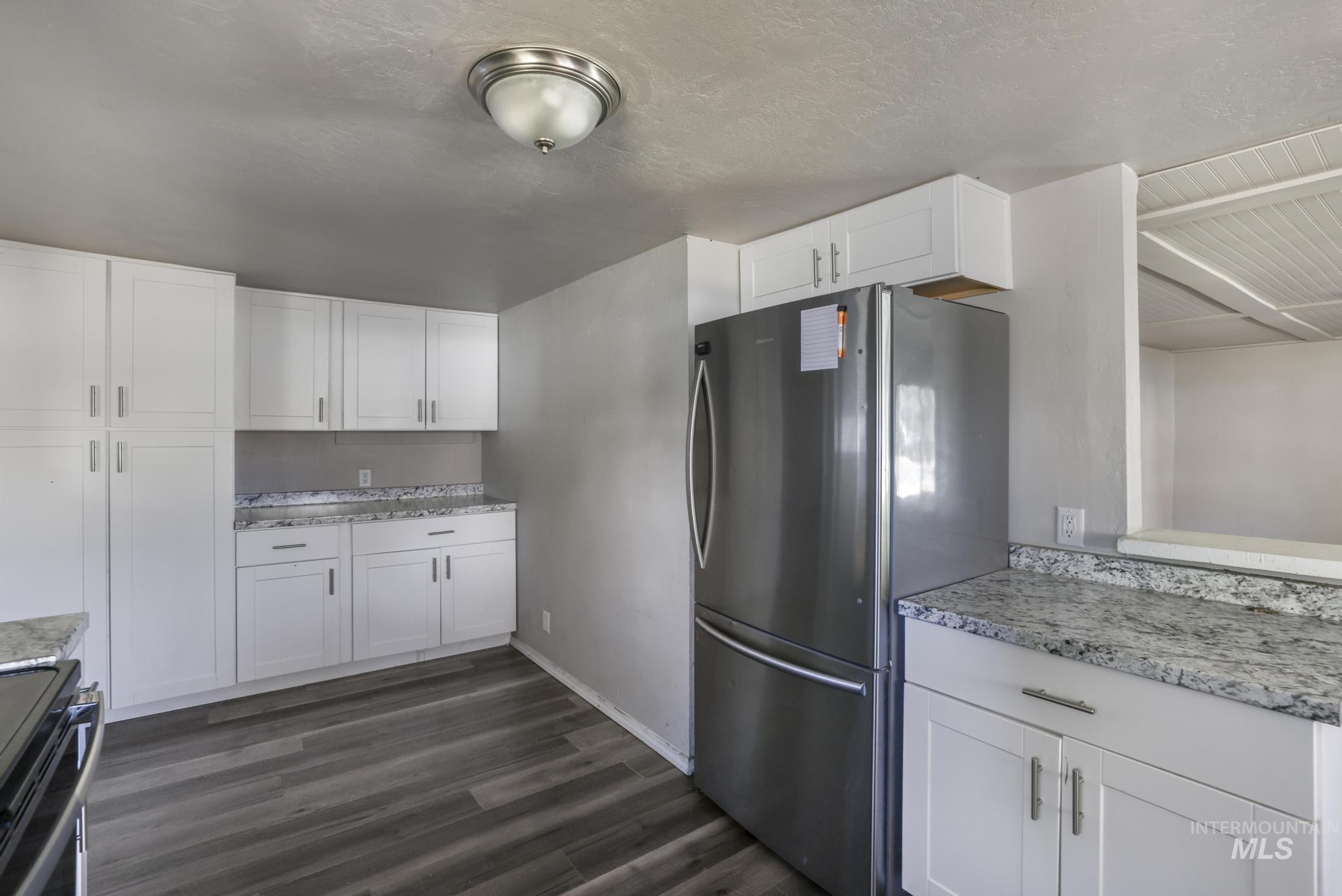 Kitchen with freestanding refrigerator, black stove, white cabinetry, dark wood-style floors, and a textured ceiling