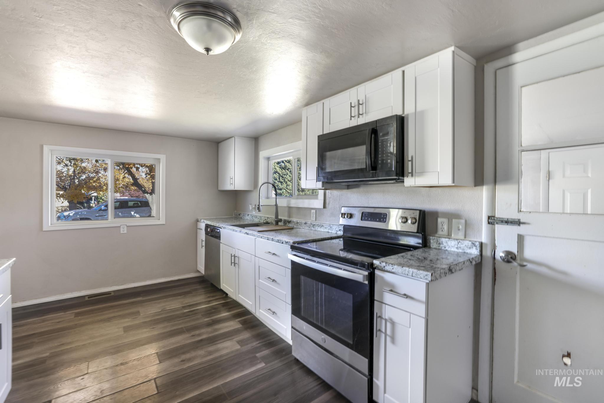 Kitchen with appliances with stainless steel finishes, white cabinets, light countertops, dark wood-type flooring, and a textured ceiling