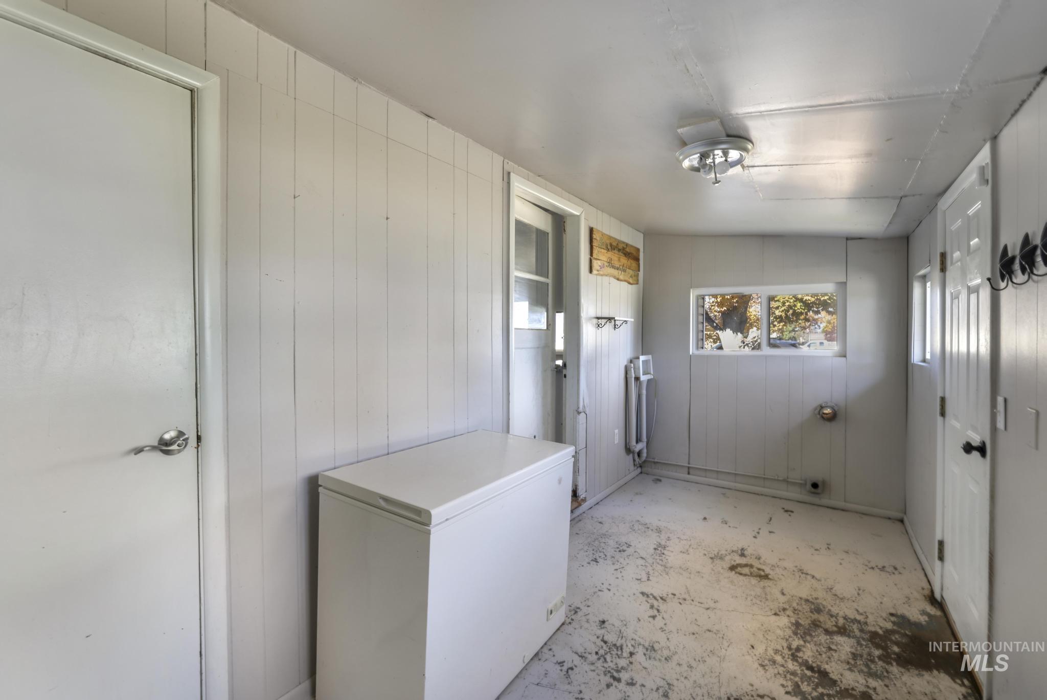 Laundry area featuring wooden walls and unfinished concrete floors