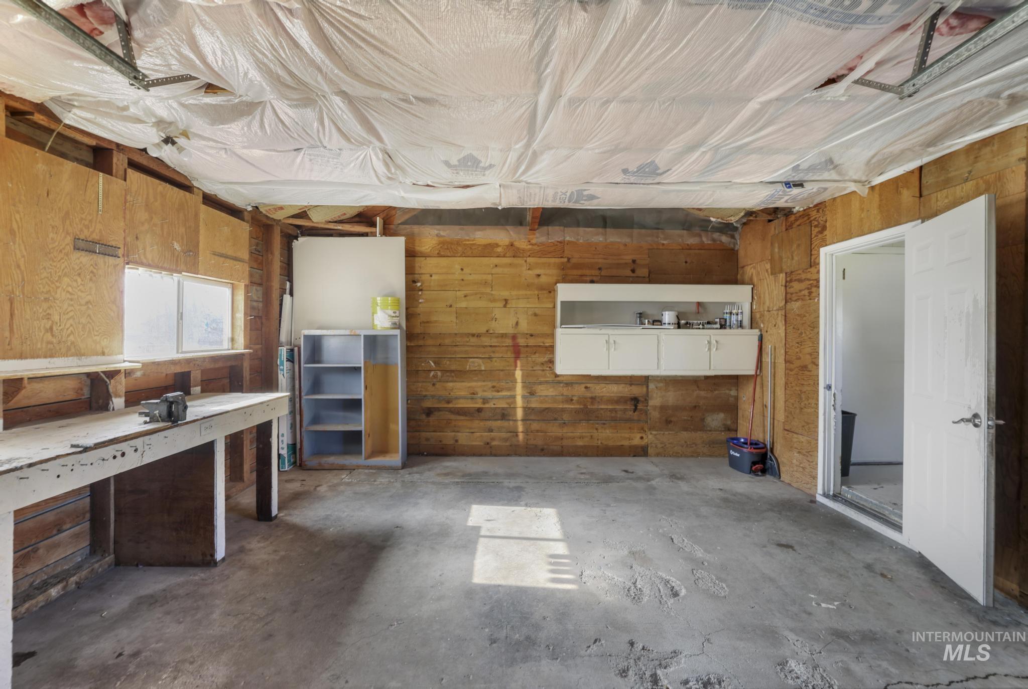 Misc room featuring wood walls, concrete flooring, a garage, and a workshop area