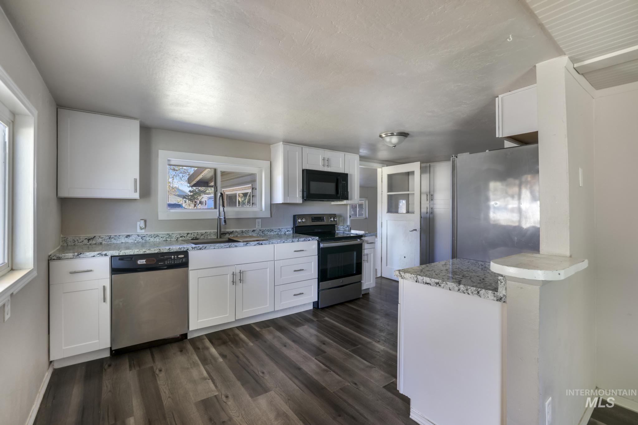 Kitchen featuring white cabinetry, stainless steel appliances, dark wood finished floors, and light stone counters