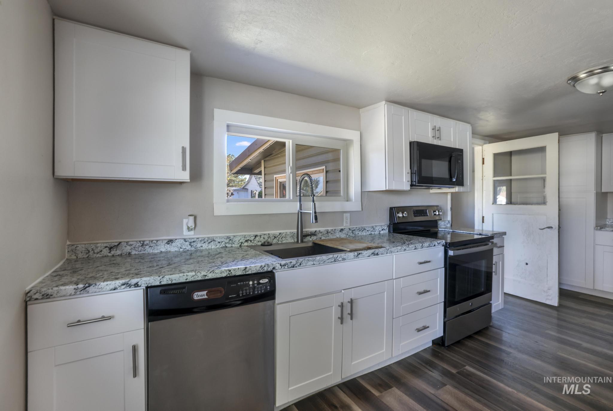 Kitchen featuring appliances with stainless steel finishes, white cabinetry, dark wood-style flooring, and light stone counters