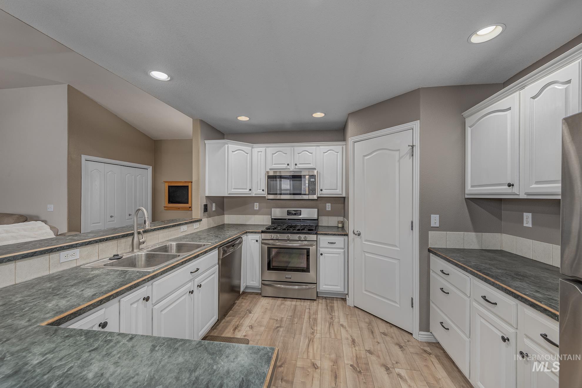 Kitchen with appliances with stainless steel finishes, white cabinets, light wood-type flooring, and recessed lighting