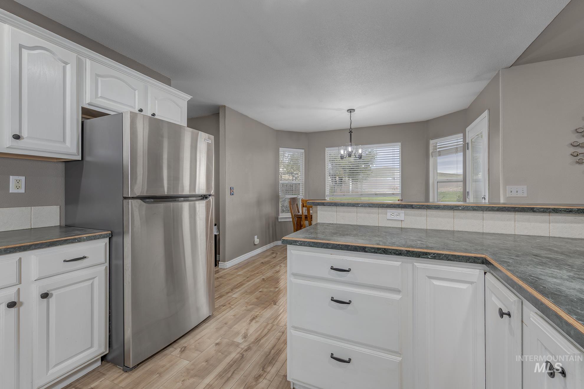 Kitchen with white cabinets, freestanding refrigerator, light wood-style flooring, and a chandelier