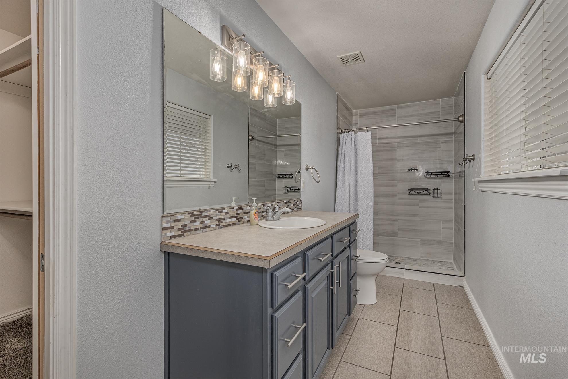 Full bathroom featuring a spacious closet, vanity, light tile patterned floors, a shower stall, and tasteful backsplash