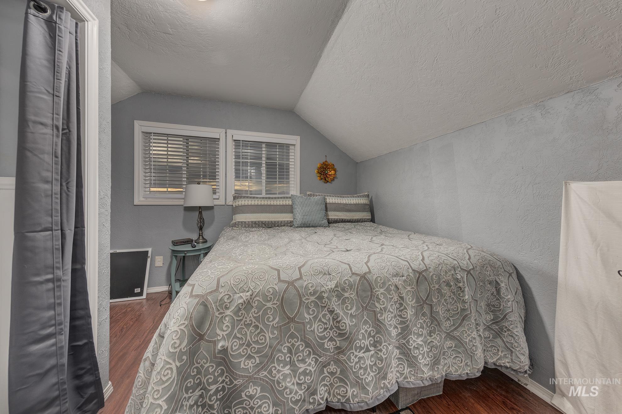 Bedroom with a textured ceiling, dark wood finished floors, vaulted ceiling, and a textured wall
