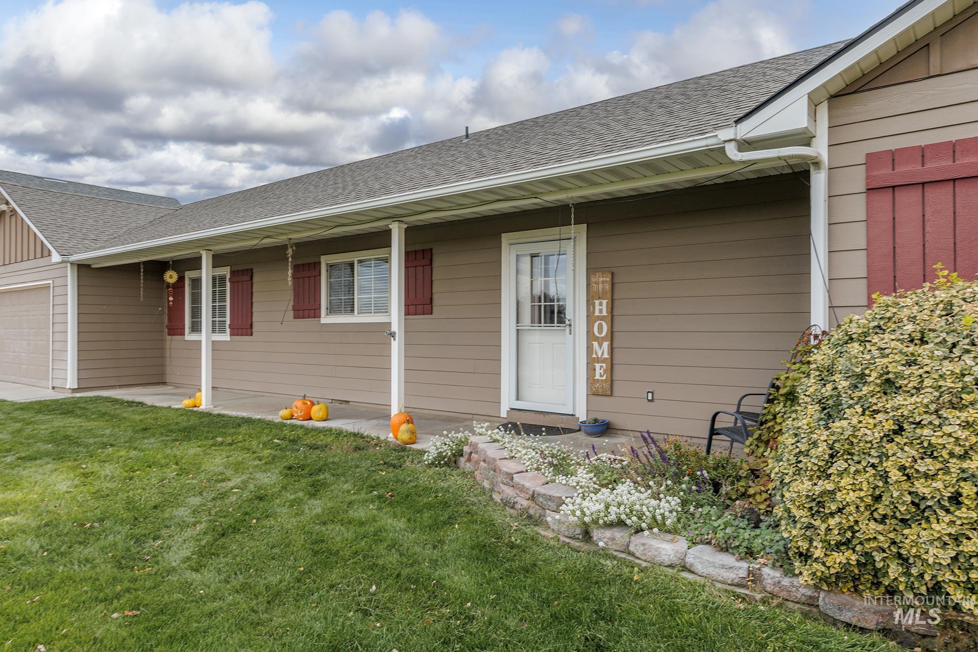 Entrance to property featuring roof with shingles, a yard, an attached garage, and a porch