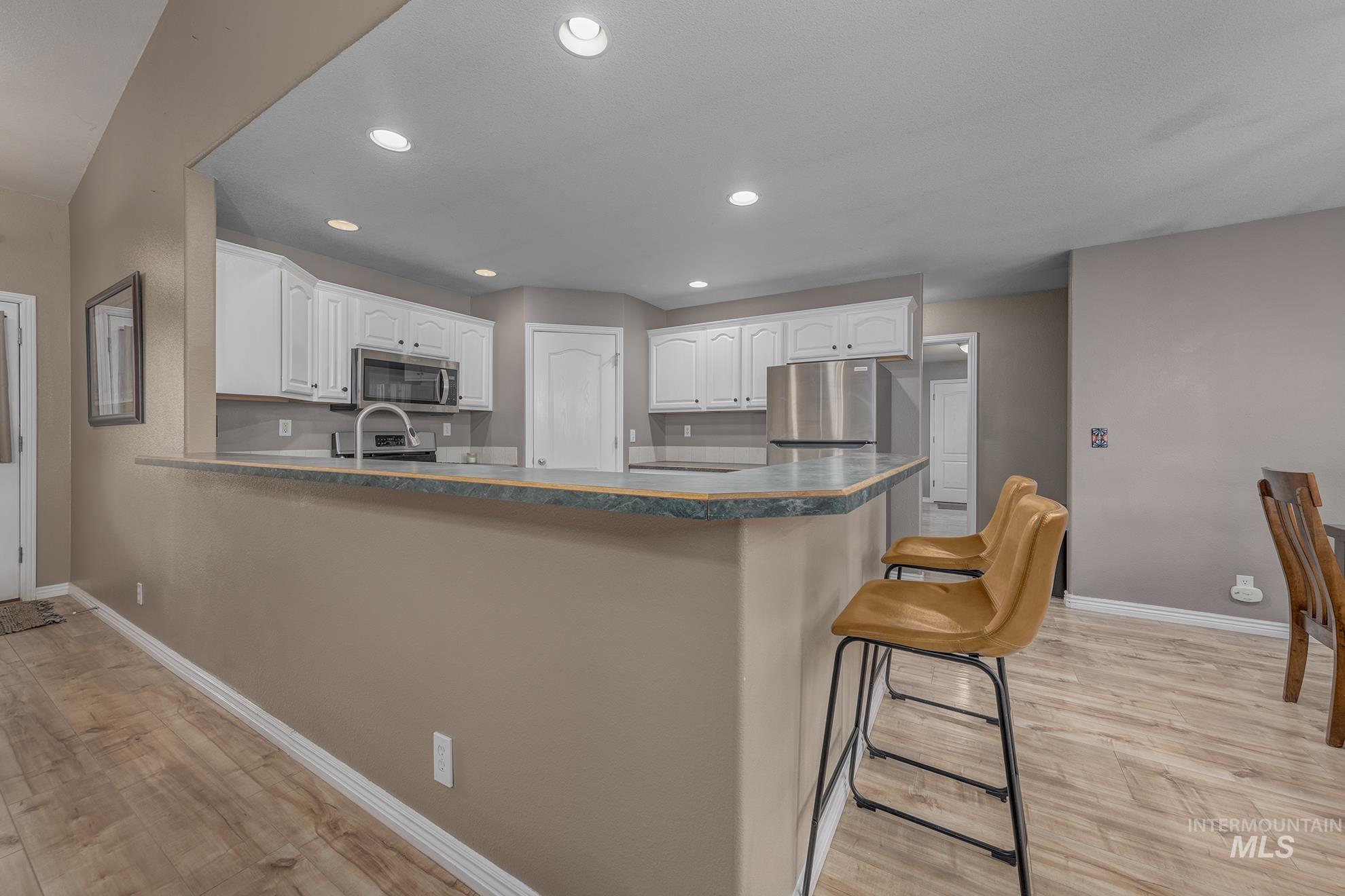 Kitchen with light wood-style floors, white cabinetry, recessed lighting, dark countertops, and a peninsula