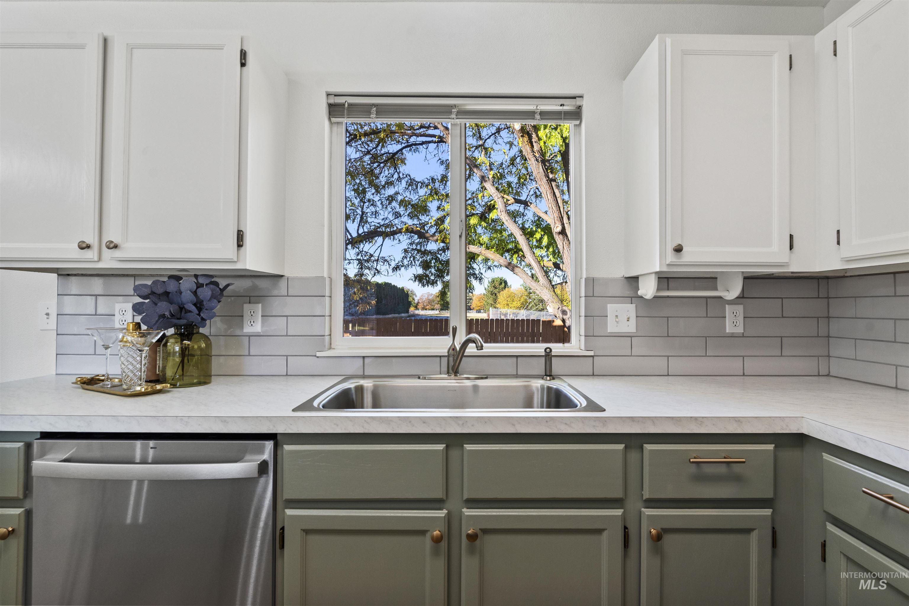 Kitchen featuring white cabinetry, stainless steel dishwasher, decorative backsplash, light countertops, and green cabinets