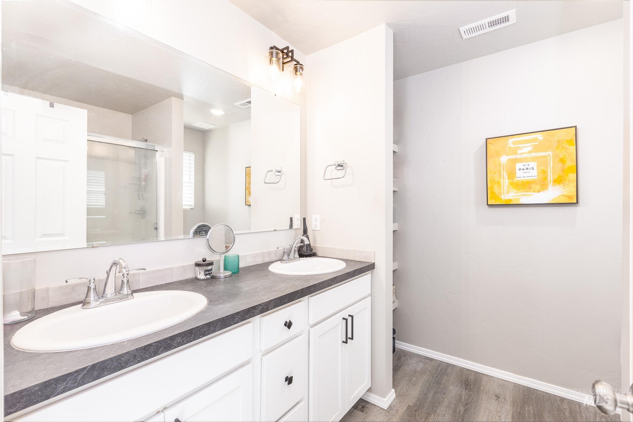 Full bath featuring a shower stall, double vanity, and light wood-style flooring