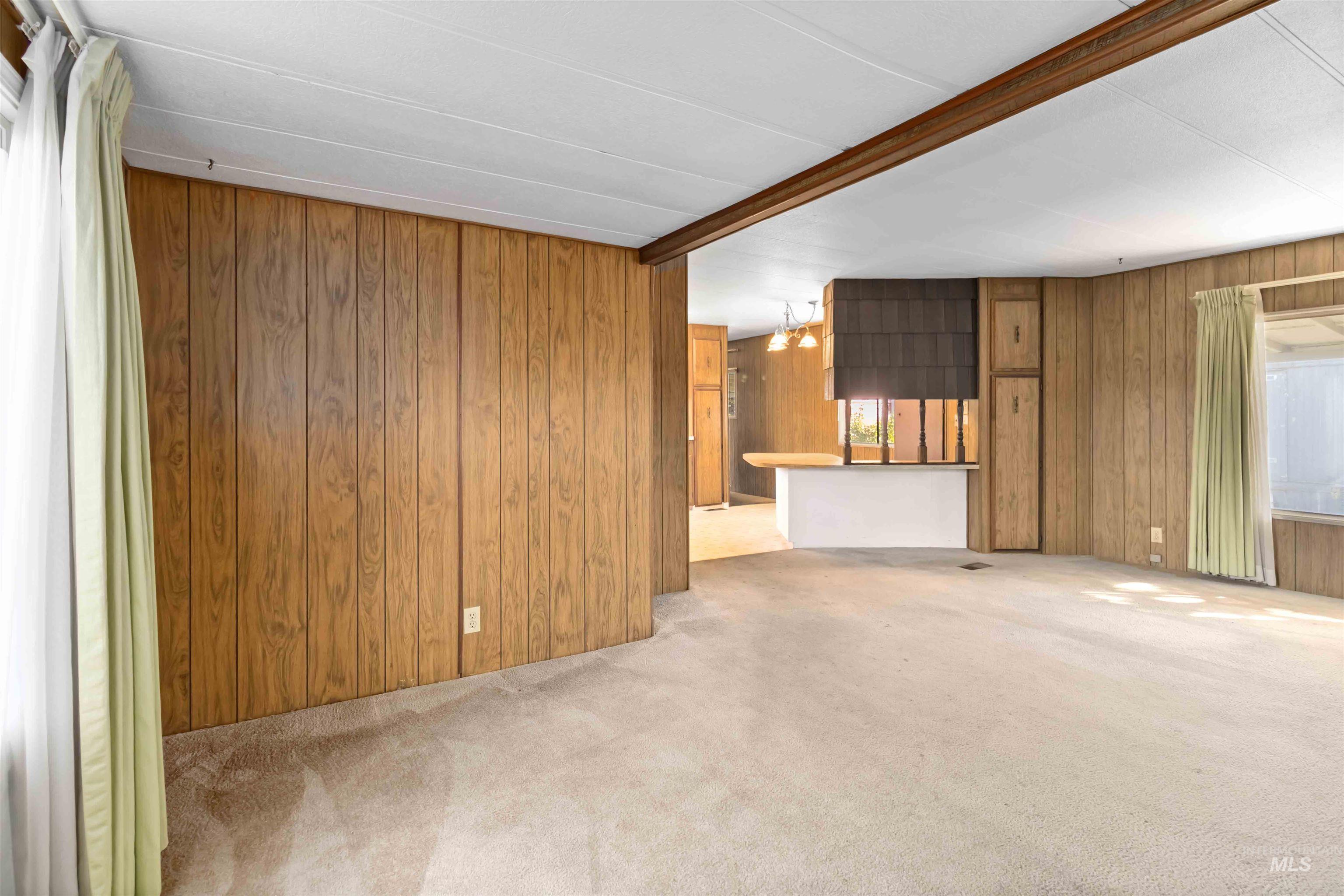 Unfurnished living room featuring wood walls, light carpet, and beamed ceiling