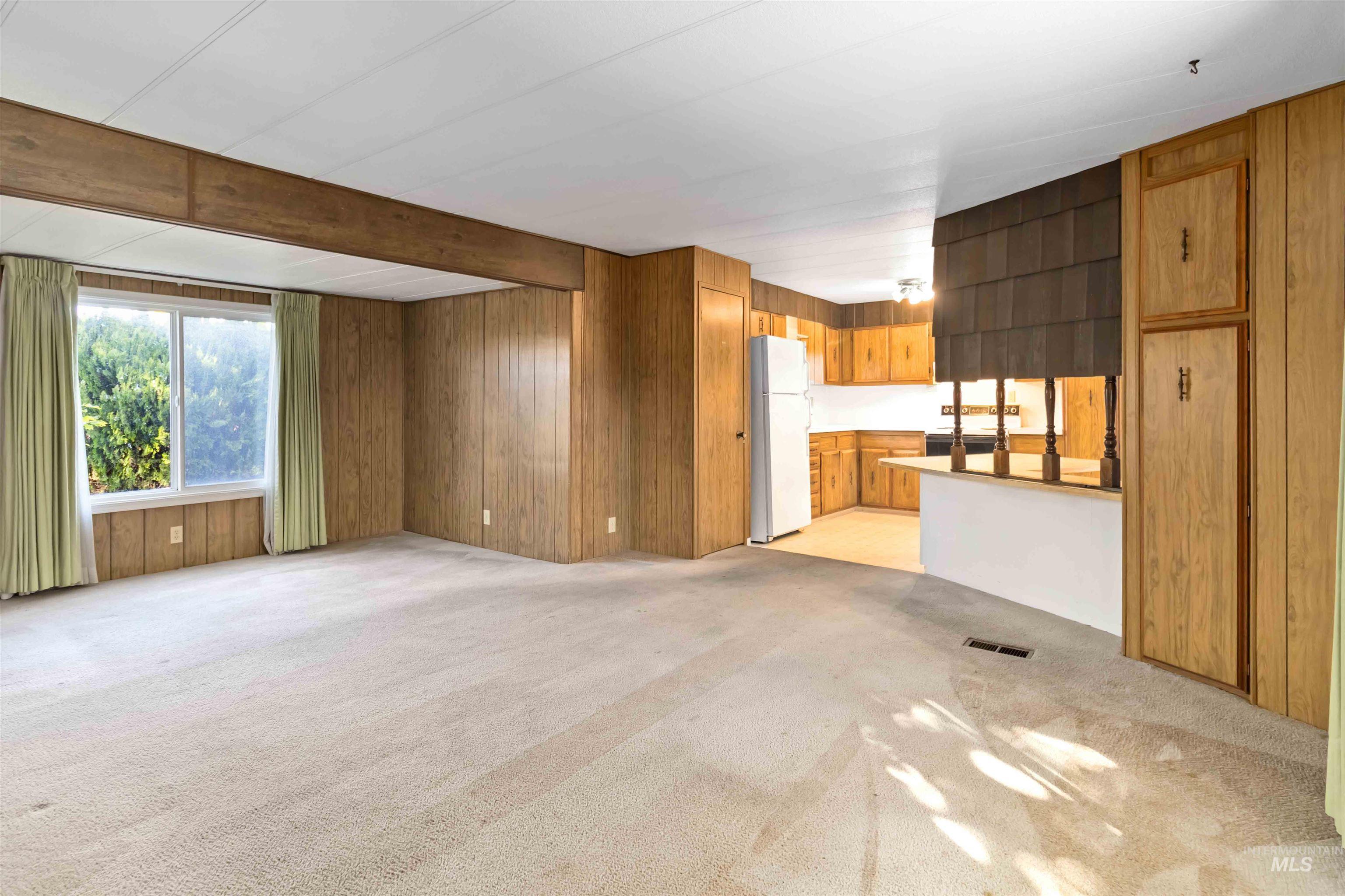 Unfurnished living room featuring beam ceiling, light carpet, and wood walls