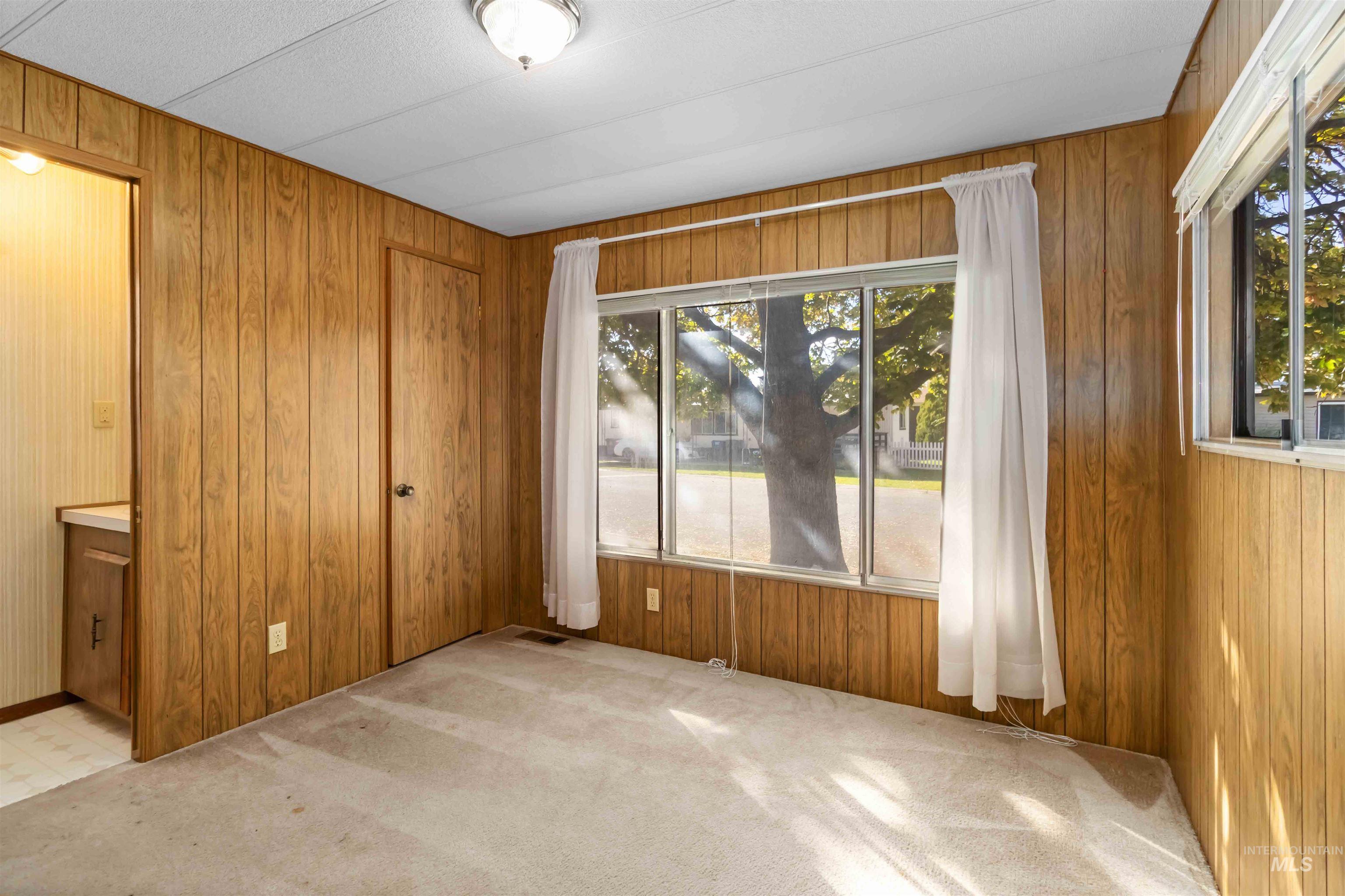 Unfurnished bedroom featuring light carpet, wood walls, and a closet