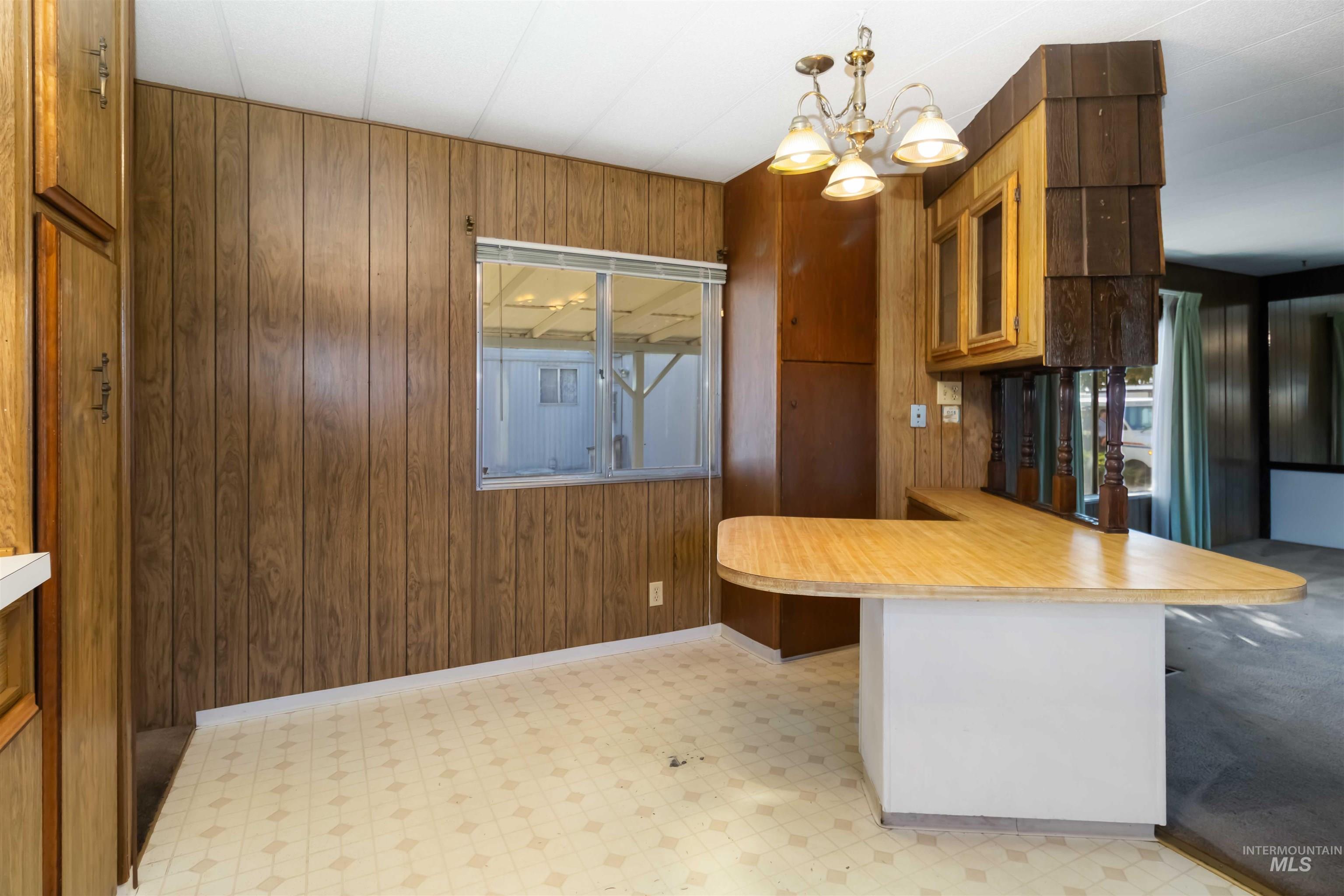 Kitchen with wooden walls, light countertops, a peninsula, light flooring, and decorative light fixtures