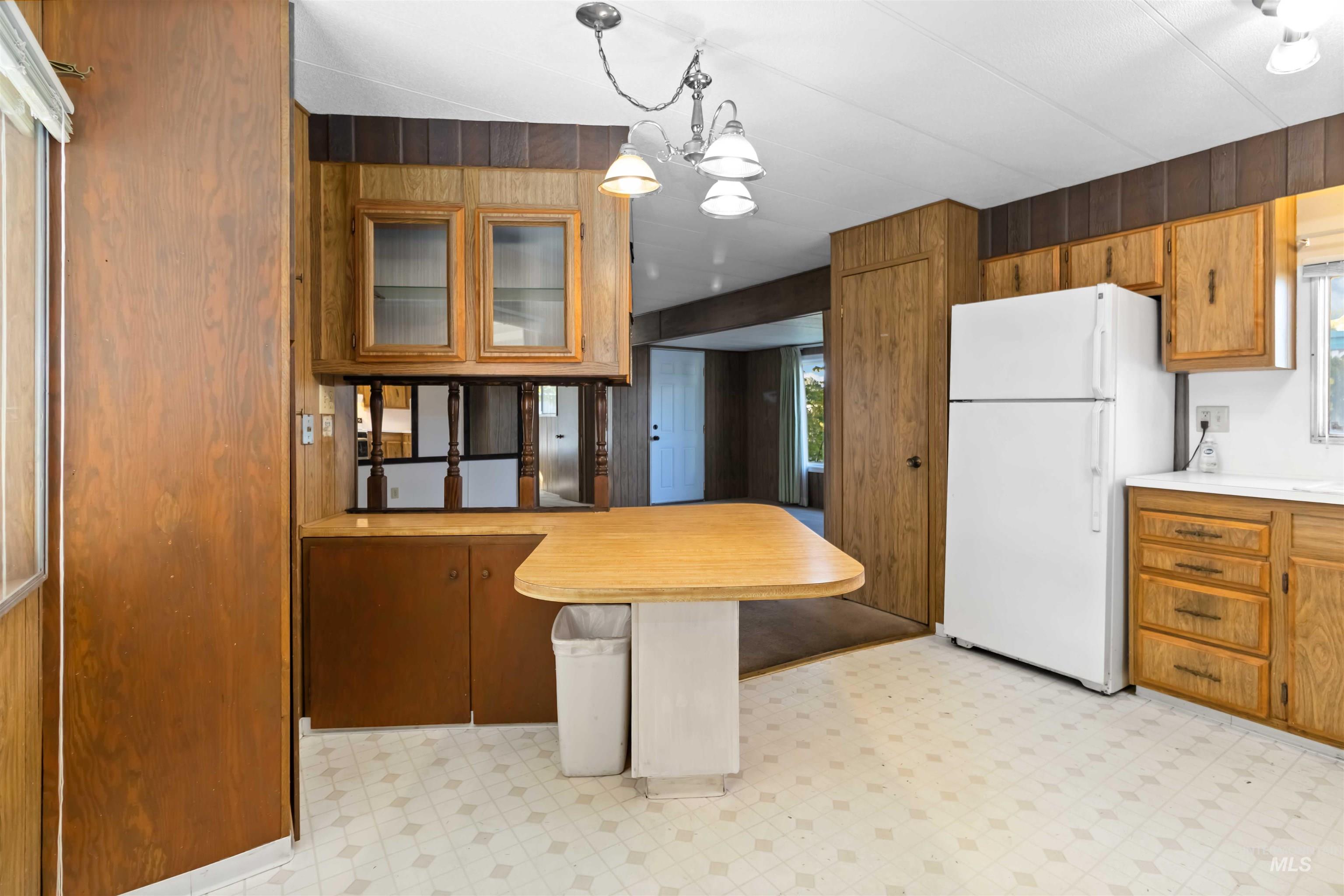 Kitchen with light flooring, brown cabinets, wooden walls, freestanding refrigerator, and decorative light fixtures
