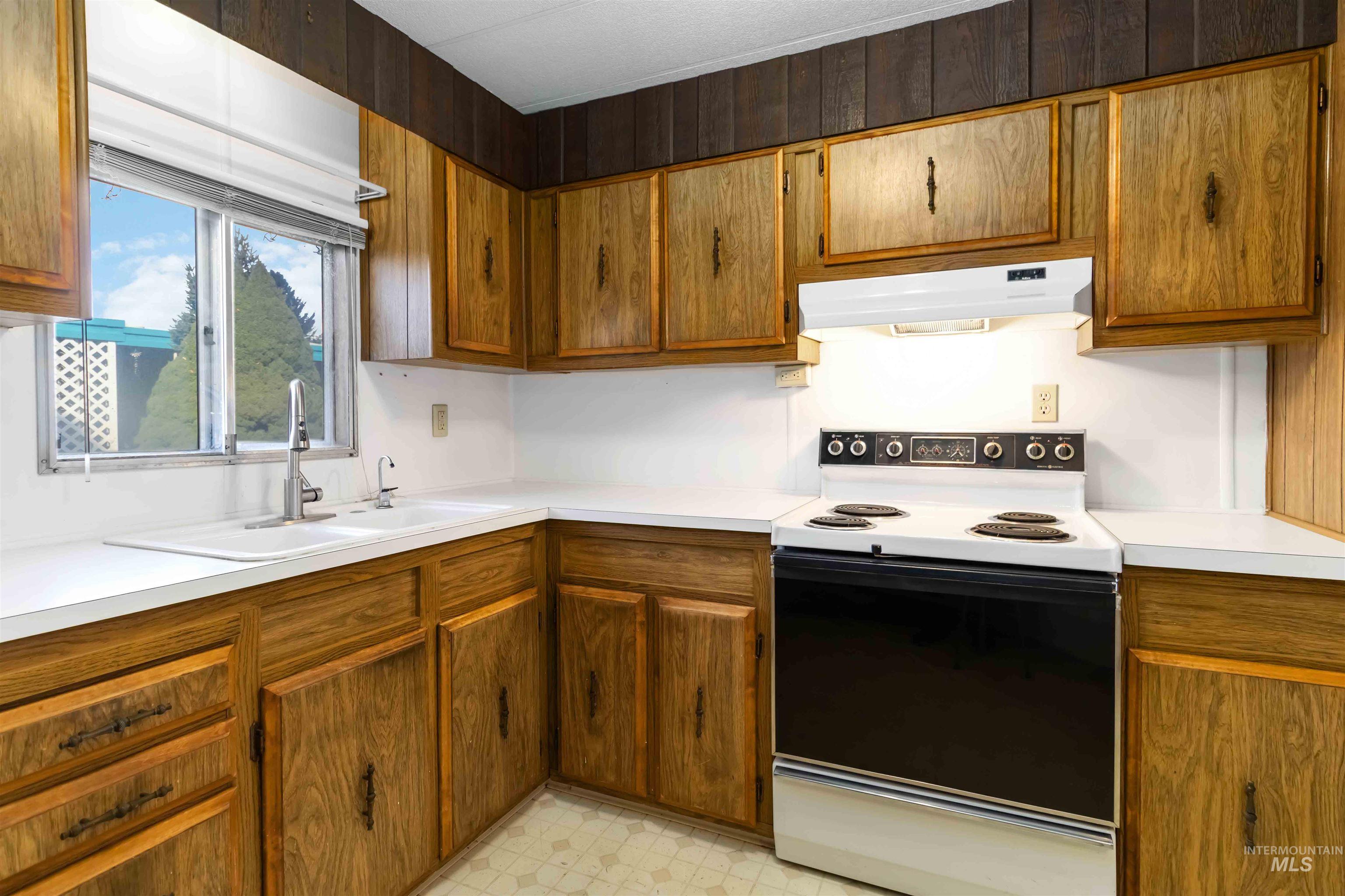 Kitchen with electric range, light countertops, and under cabinet range hood