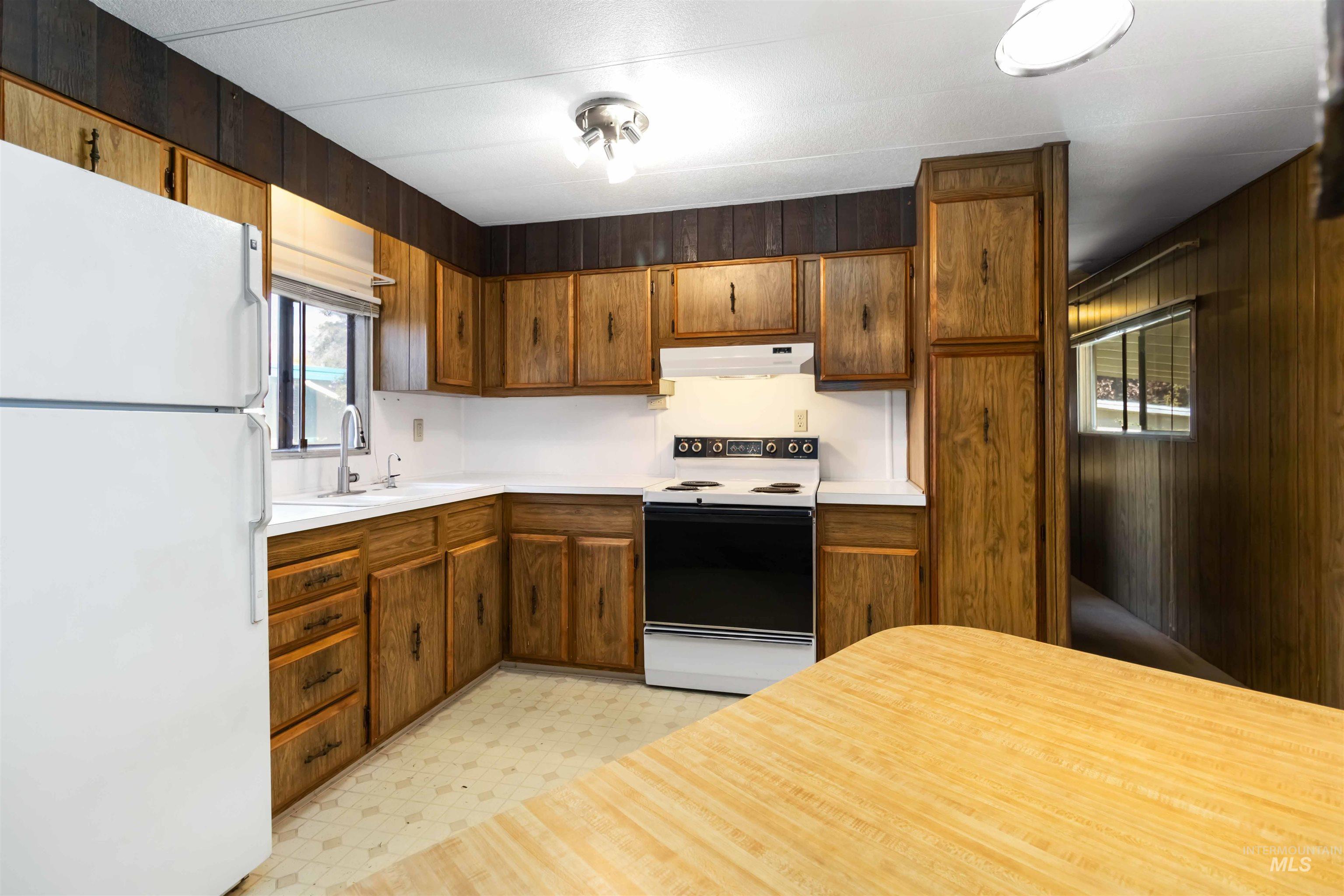 Kitchen with white appliances, wood walls, light countertops, light floors, and under cabinet range hood