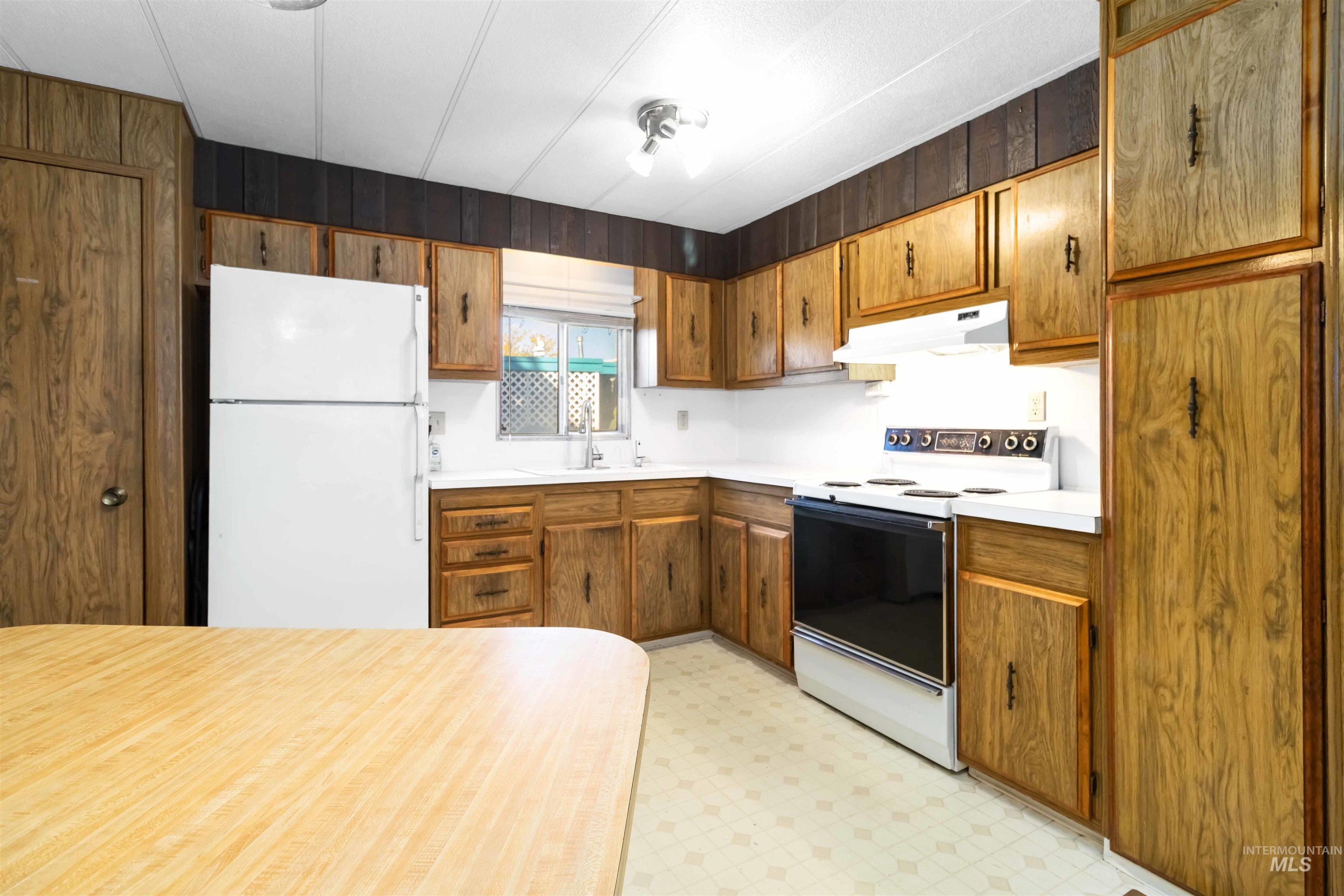 Kitchen featuring white appliances, light countertops, light floors, brown cabinetry, and under cabinet range hood