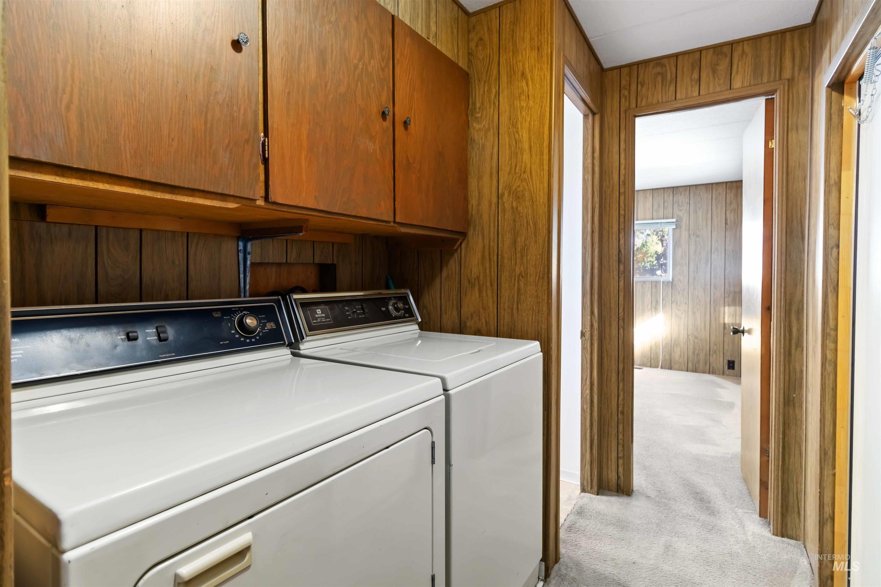 Washroom featuring light carpet, wooden walls, washer and clothes dryer, and cabinet space